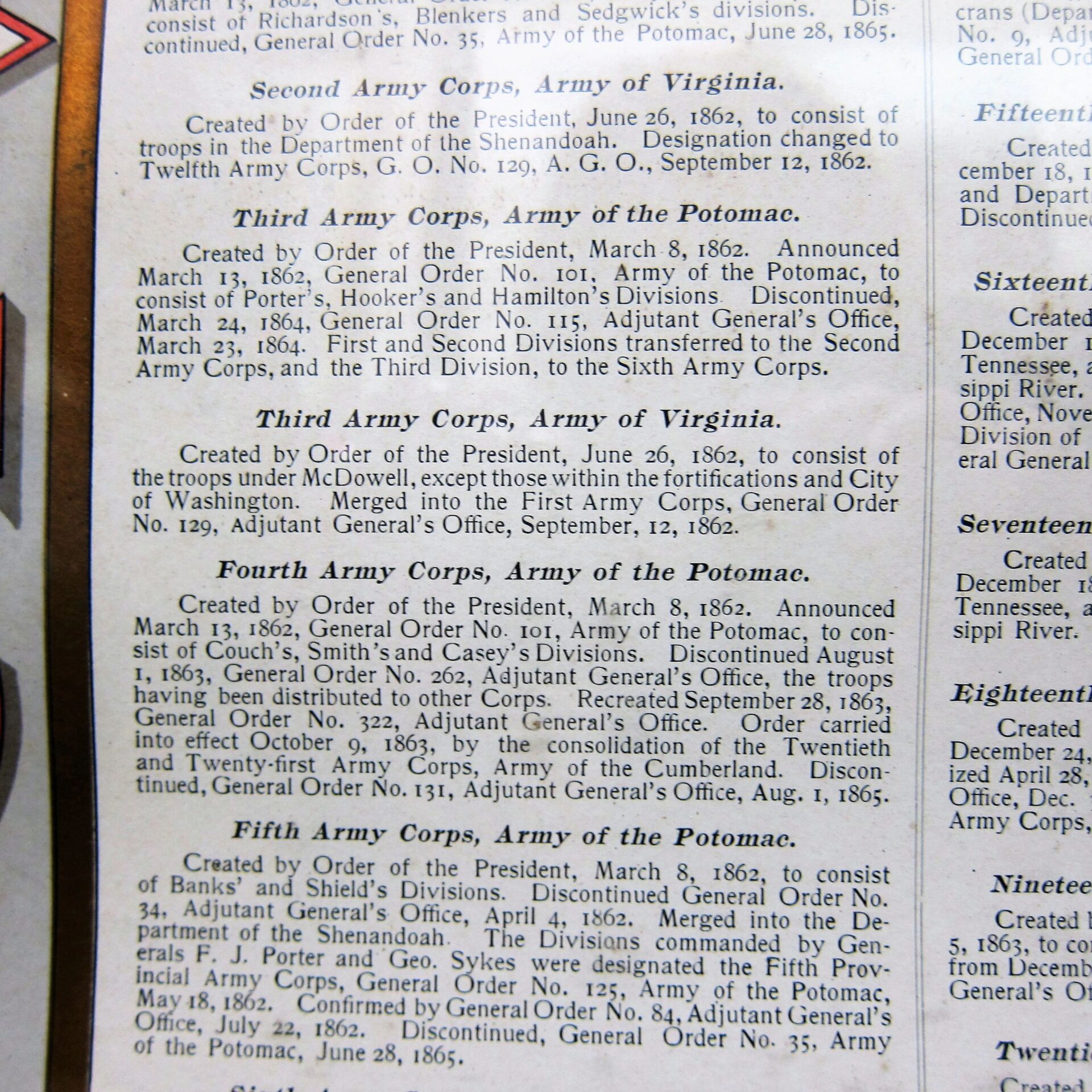 A close-up photo of a US Army Corp Escutcheon beside a book page detailing historical orders for the Second through Fifth Army Corps, including dates and official references.