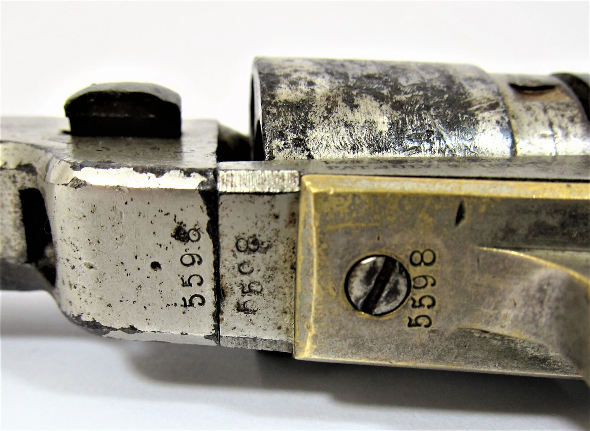 Close-up of a Colt Wells Fargo Conversion showing serial number 55998 stamped on multiple parts, including a brass section with a screw and a worn cylindrical metal component.