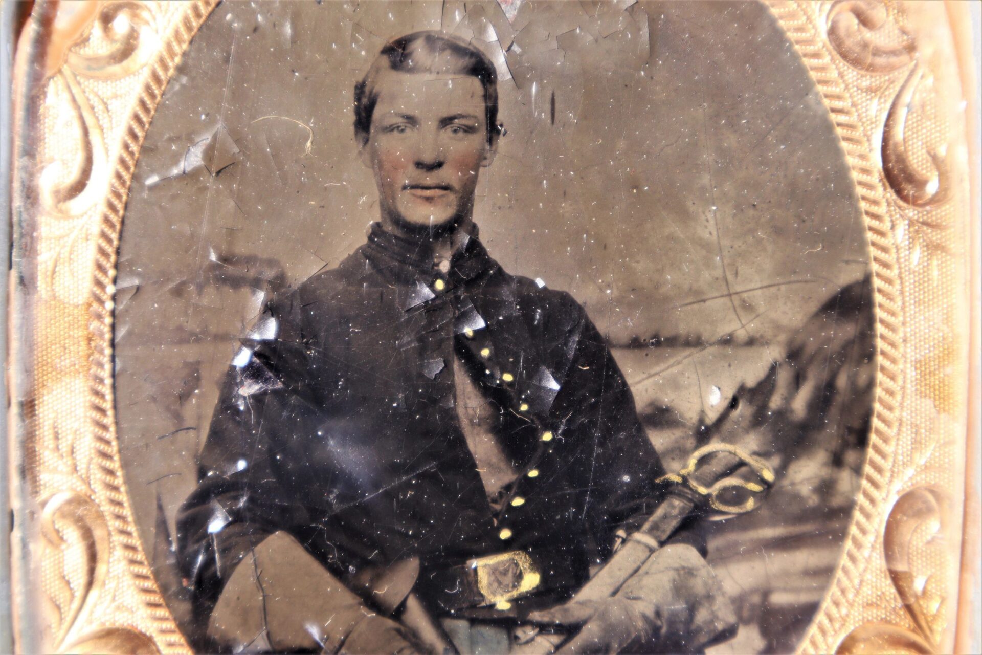 Cavlary Image: Tintype photograph of a young man in a Civil War-era military uniform holding a sword, displayed in an ornate frame with visible scratches and surface damage.