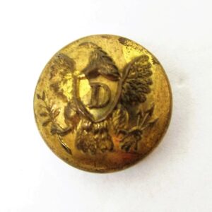 The US Dragoon Button is a round, gold-colored button featuring an eagle with outstretched wings holding a shield engraved with the letter "D" in the center.