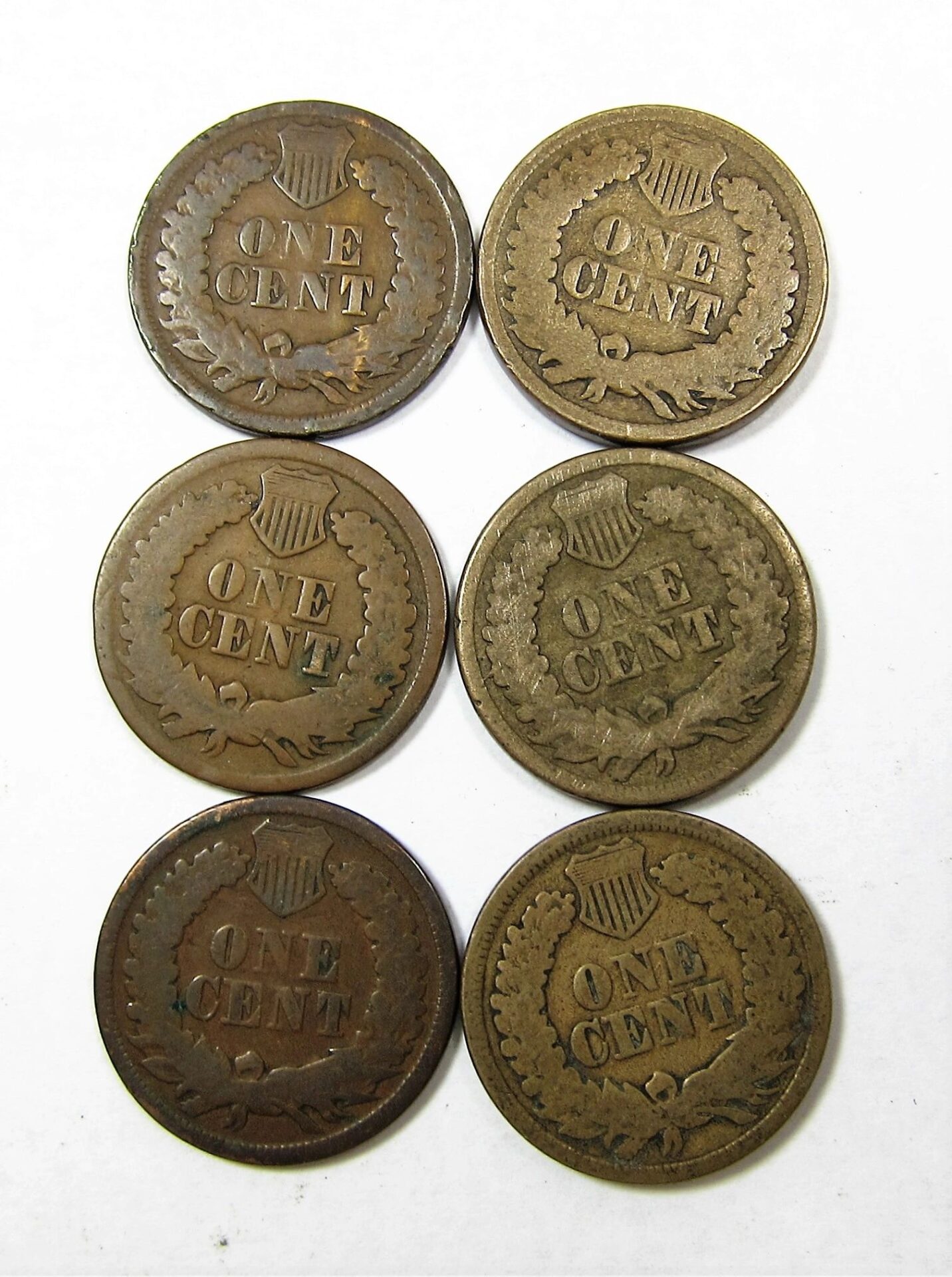 Six Indian Head One Cent vintage coins, featuring a wreath and shield design, are arranged in two columns on a white background.