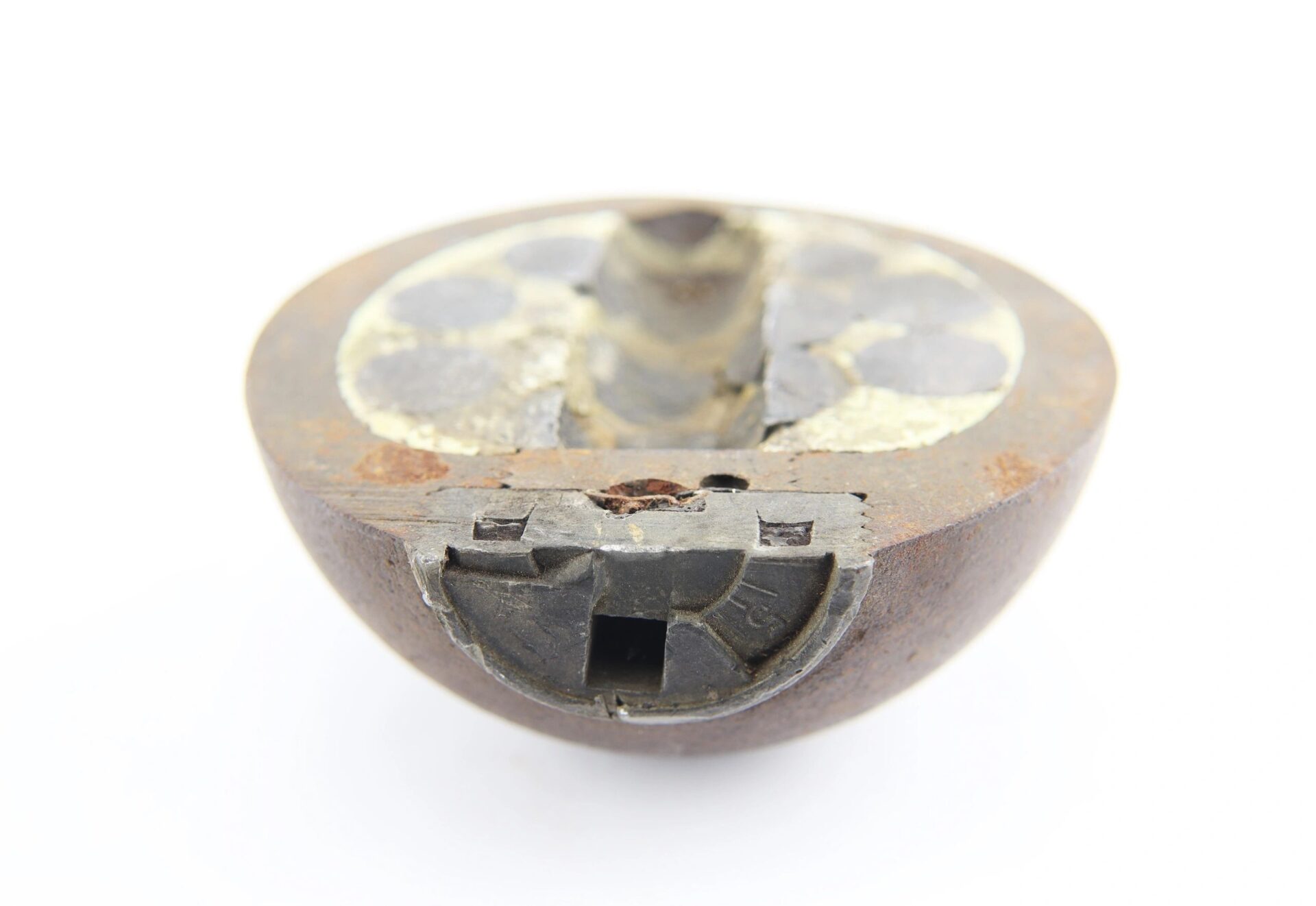 A close-up of a Confederate 6 Pound Borman artillery shell, rusted and partially disassembled to reveal its circular form and internal components, set against a white background.