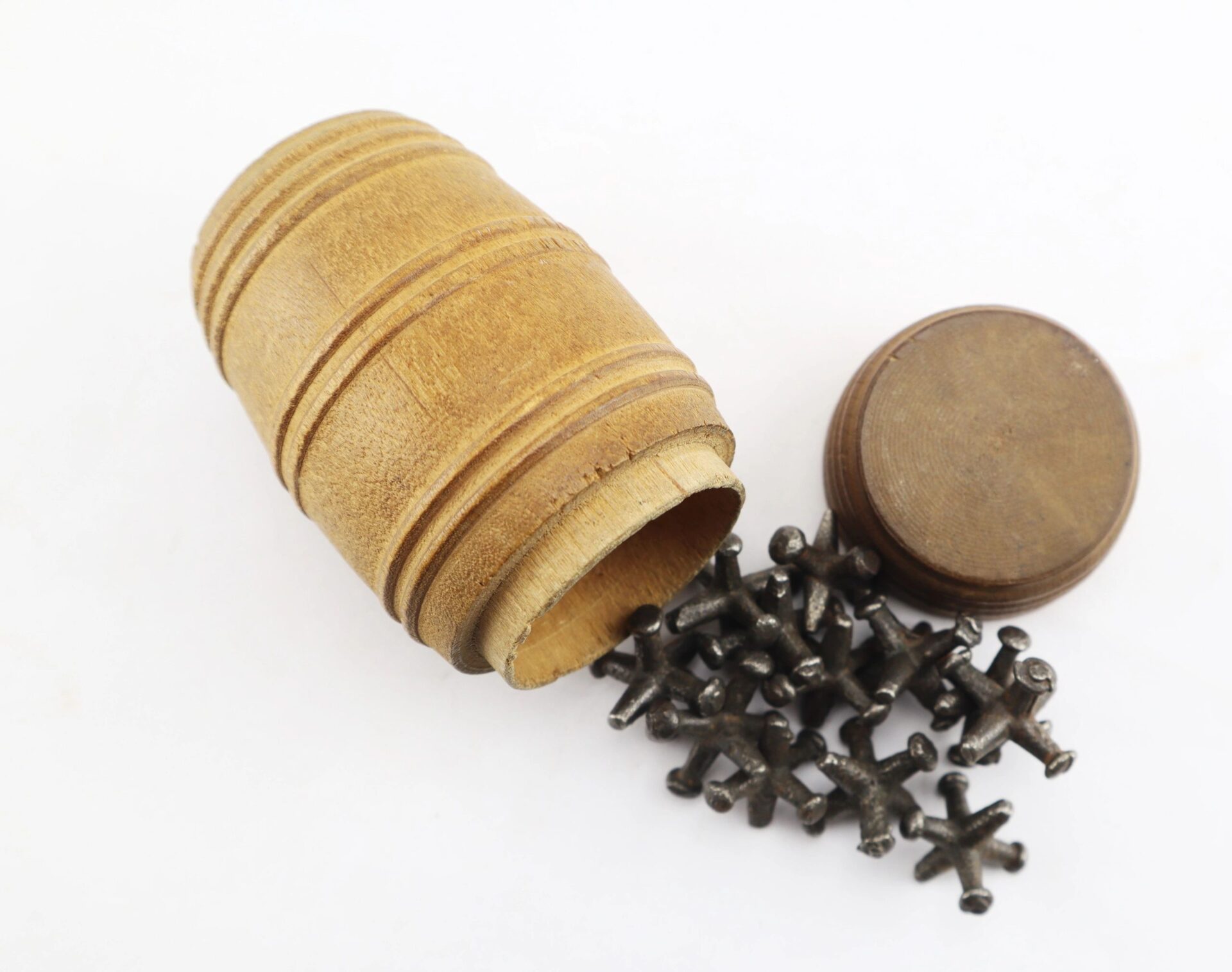 A barrel-shaped wooden container labeled "Knucklebones / Sold" lies open, with several metal knucklebones spilled beside the lid.
