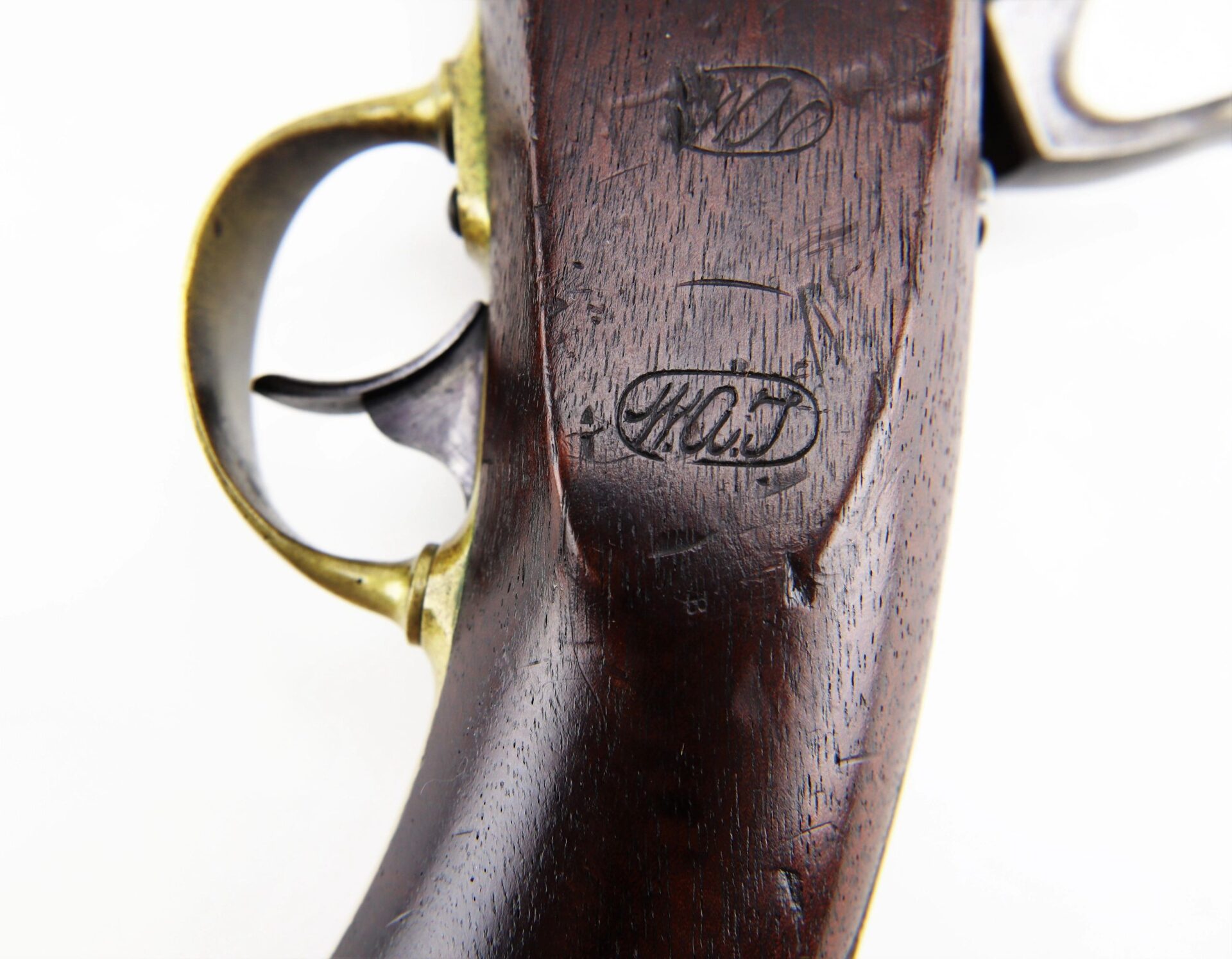 Close-up of the Aston Horse Pistol's wooden stock, highlighting its brass trigger guard and stamped oval markings.