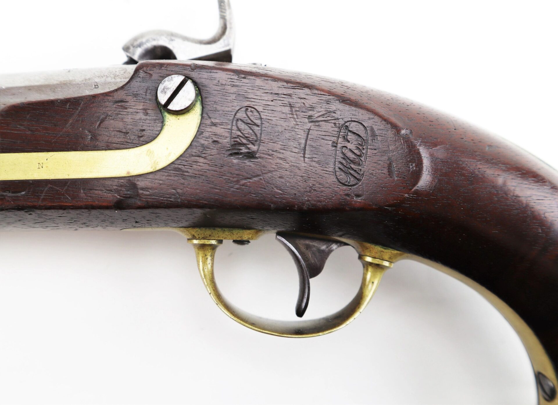 Close-up of an Aston Horse Pistol’s wooden grip and brass trigger guard, displaying engraved manufacturer’s marks on the wood.