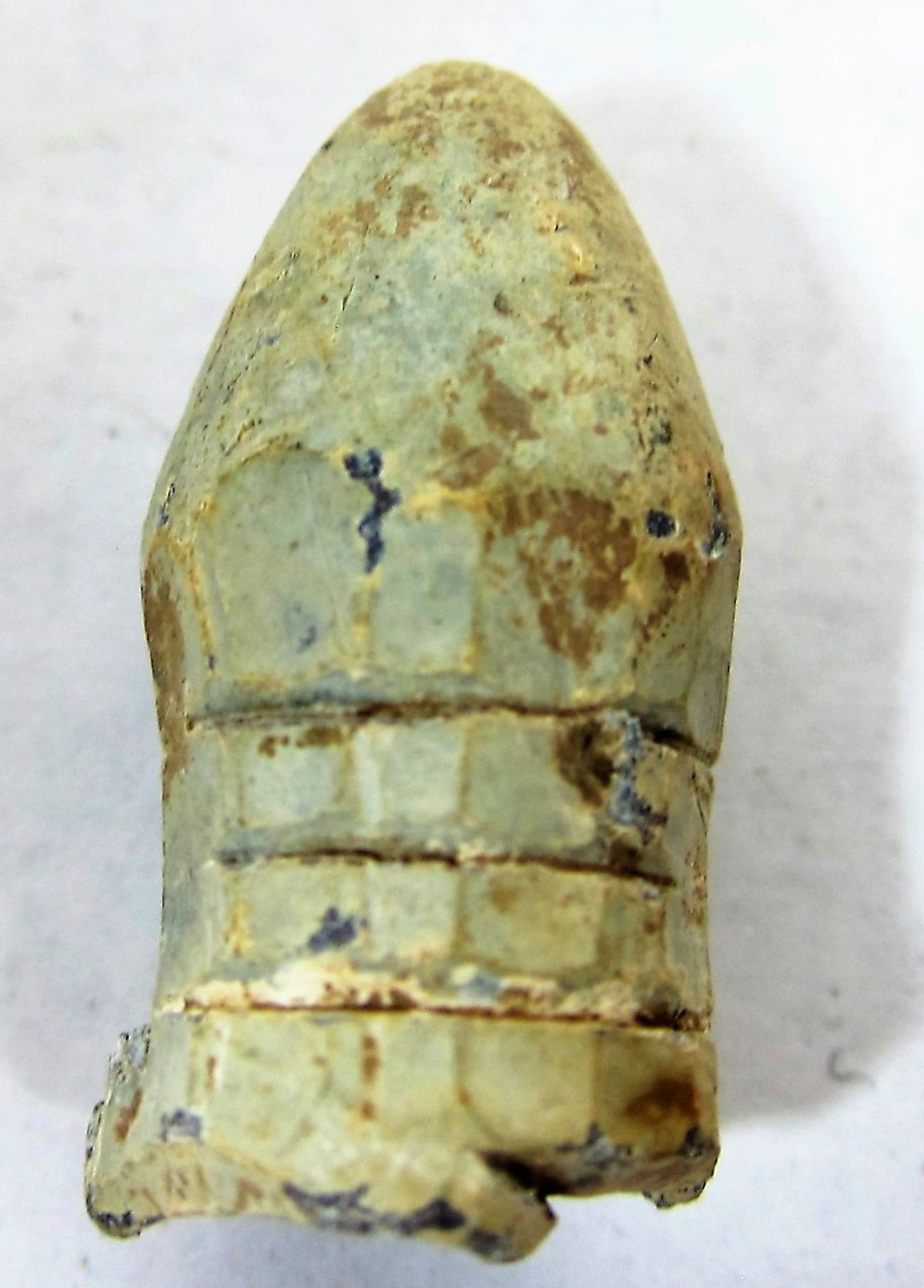 Close-up of a weathered Civil War Carved Bullet with visible grooves and surface discoloration, set against a plain background.