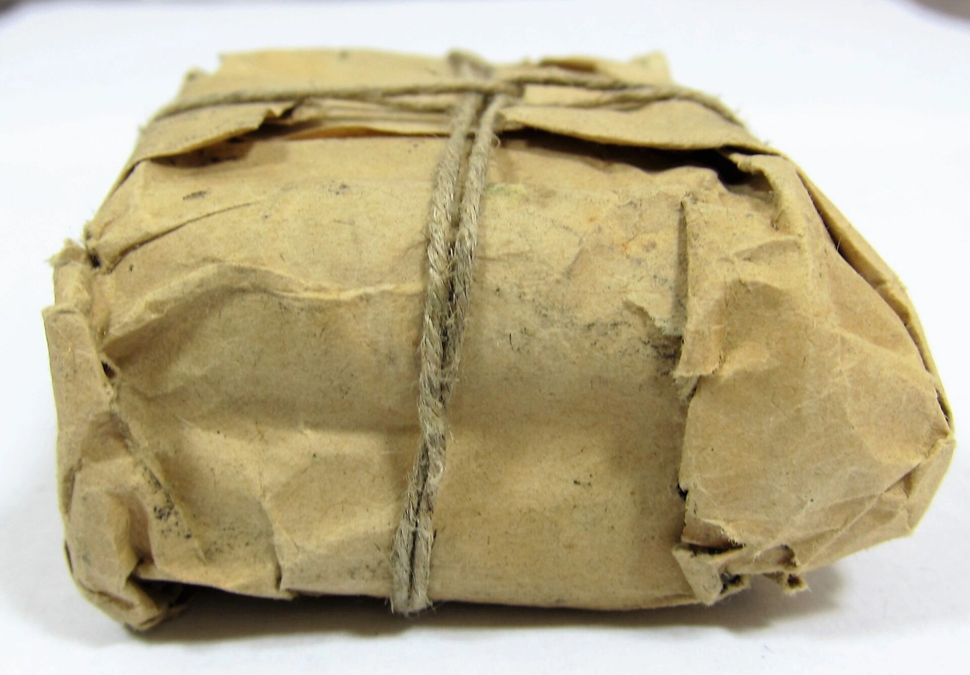 A Maynard Carbine Cartridge, rectangular and compact, wrapped in brown paper and tied with twine, rests on a white surface.