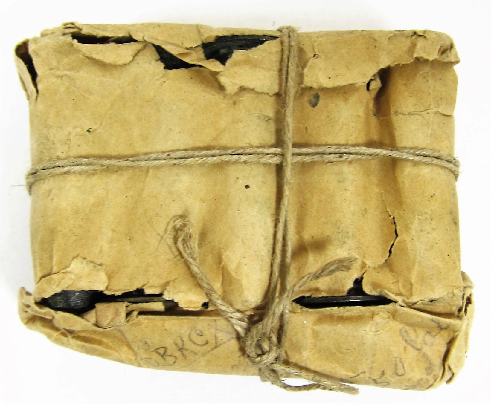 A small rectangular package labeled "Maynard Carbine Cartridge," wrapped in crumpled brown paper, tied with coarse string, with dark cartridges partially visible through torn spots.