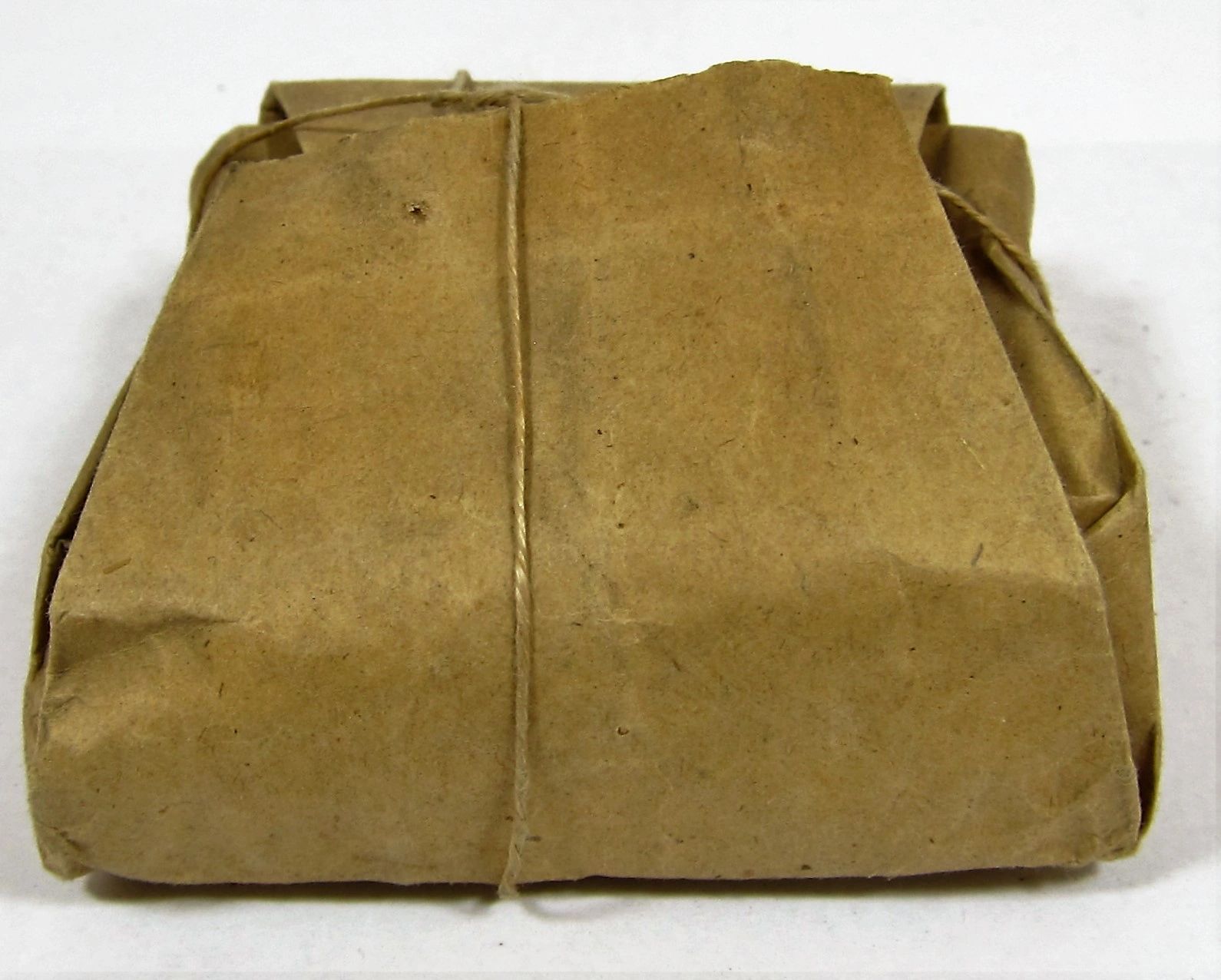 A .58 Caliber Minie Ball Paper Wrapper, rectangular and wrapped in brown paper with string, is displayed on a plain white surface.
