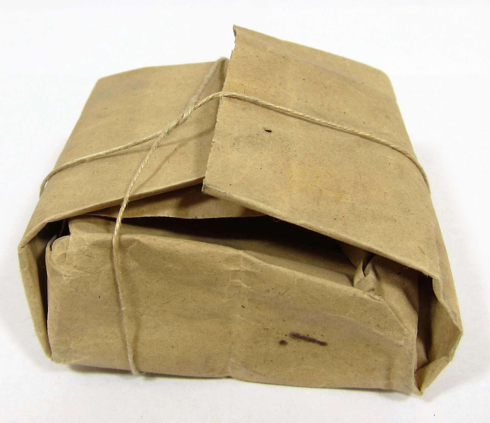 A .58 Caliber Minie Ball Paper Wrapper, rectangular and wrapped in brown paper with string, rests on a white surface.