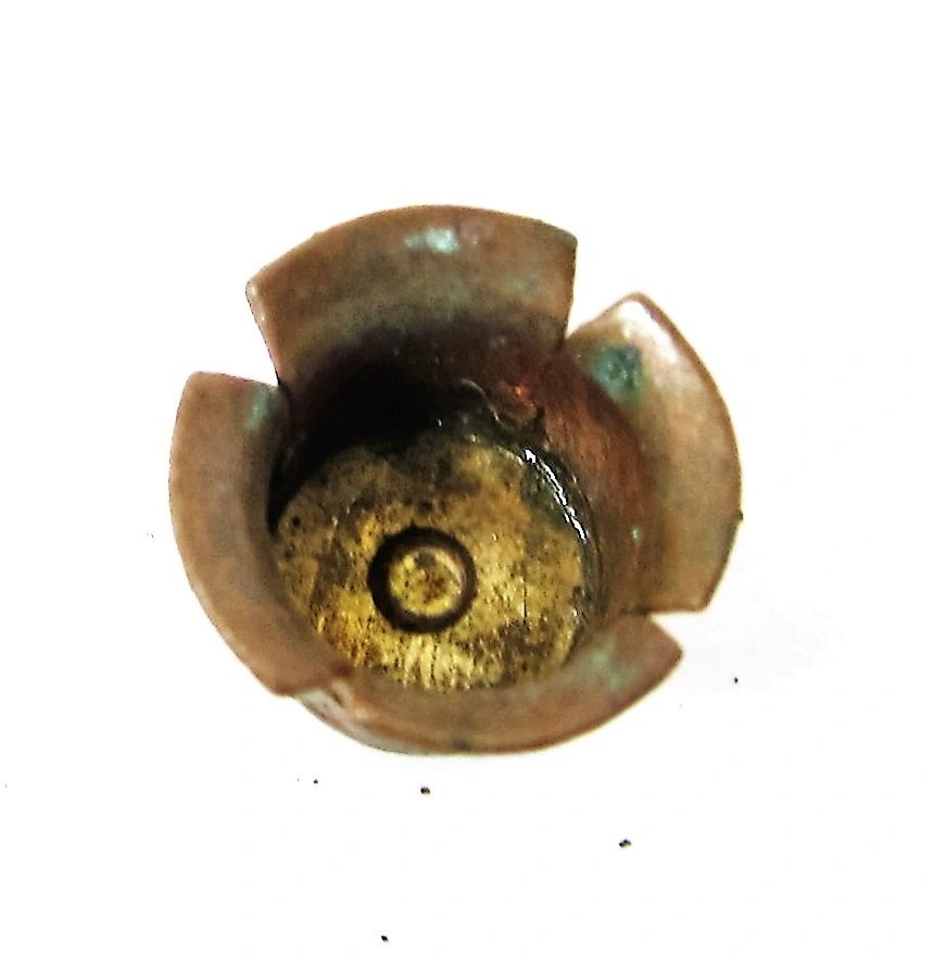 Close-up of a Percussion Cap viewed from above, displaying a flower-like pattern with a circular indentation at the center.