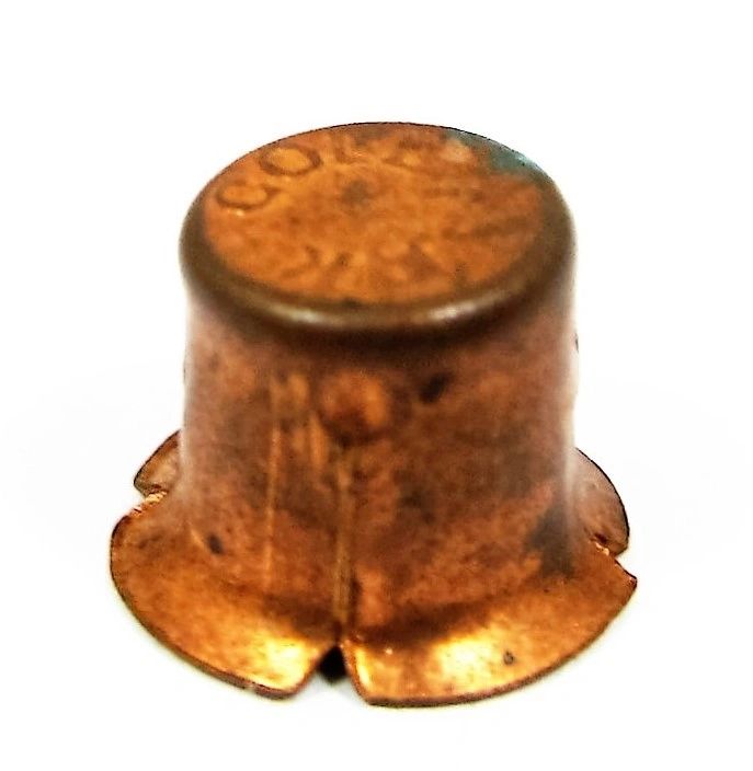A close-up of a single spent Percussion Cap with a flared base, displayed against a white background.