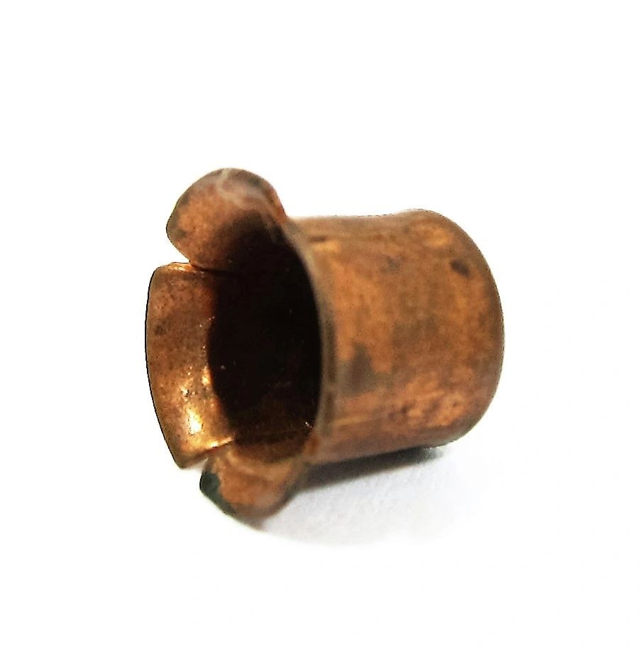A close-up photo of a small, empty, deformed Percussion Cap with flared edges, placed on a white background.