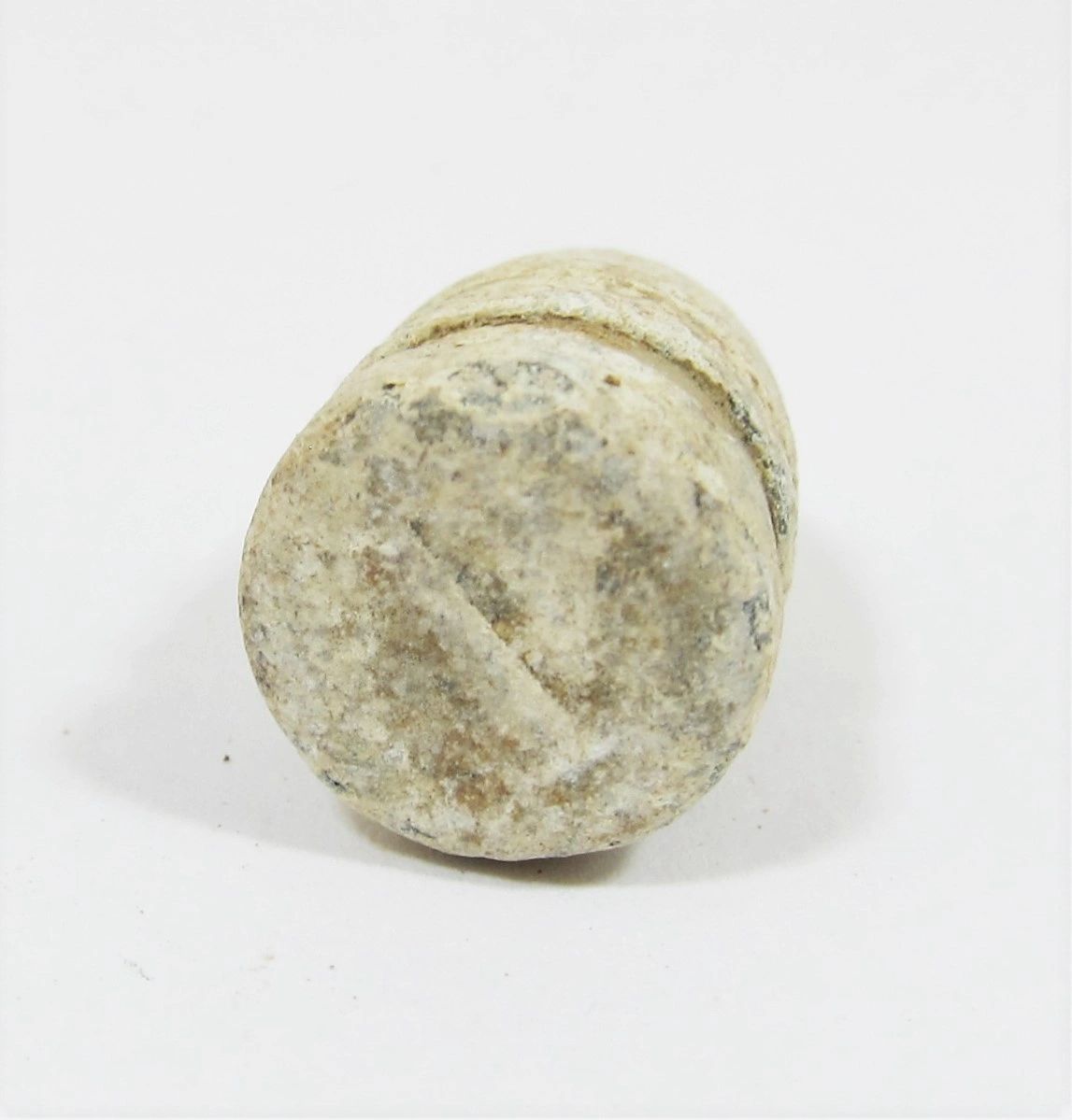A close-up of a weathered Carbine Bullet From Gettysburg, cylindrical in shape, rests on a white surface with faint markings on its flat end.