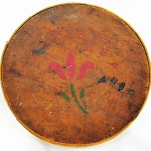 The Painted "Cheesebox" Canteen features a round, wooden surface with a faded red flower and green leaves at the center, displaying visible signs of wear and age.