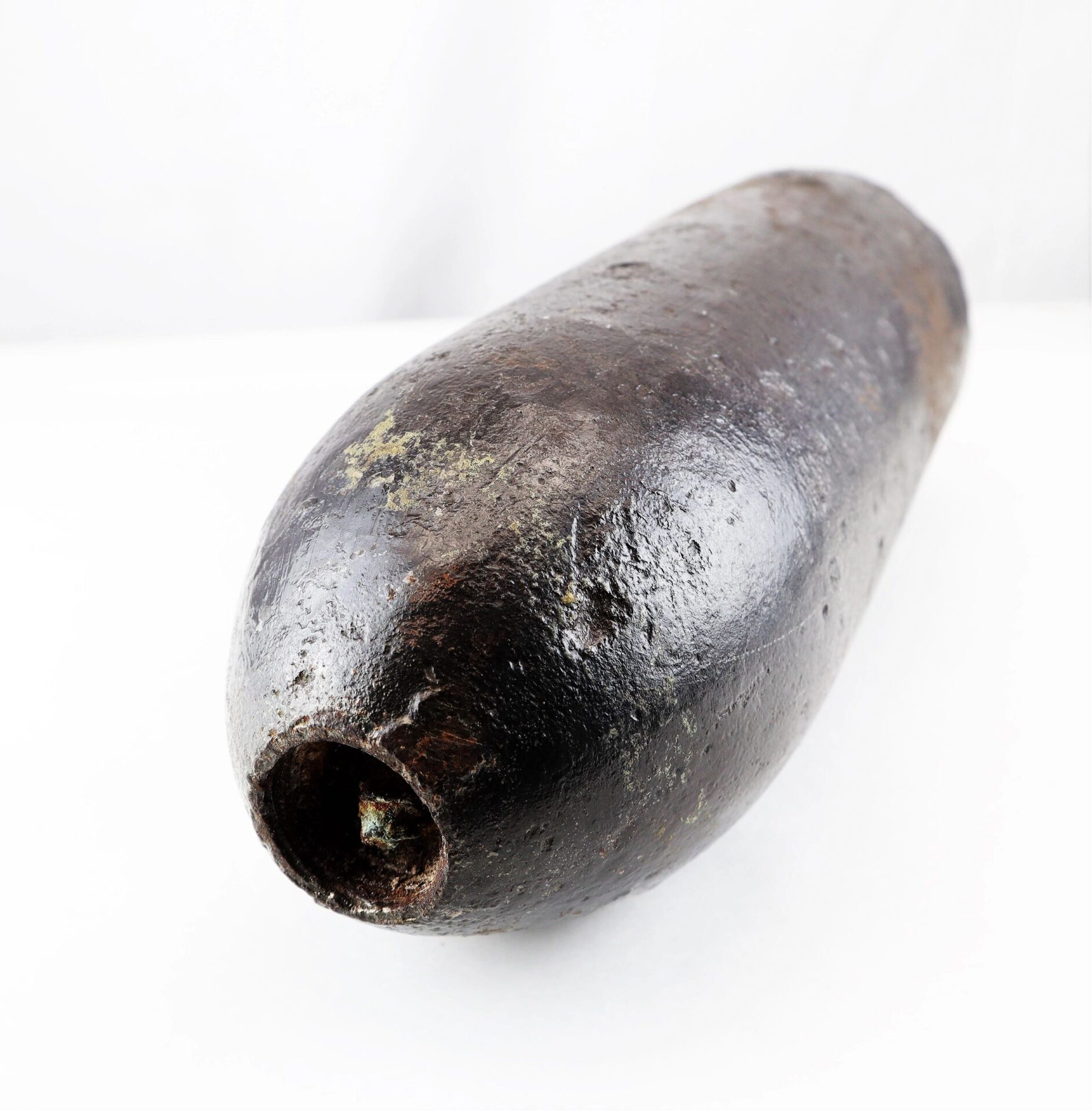 A US 4.2” 30-Pounder Parrott Common Shell with a cylindrical body and rounded tip, showing rust, rests on a white surface.