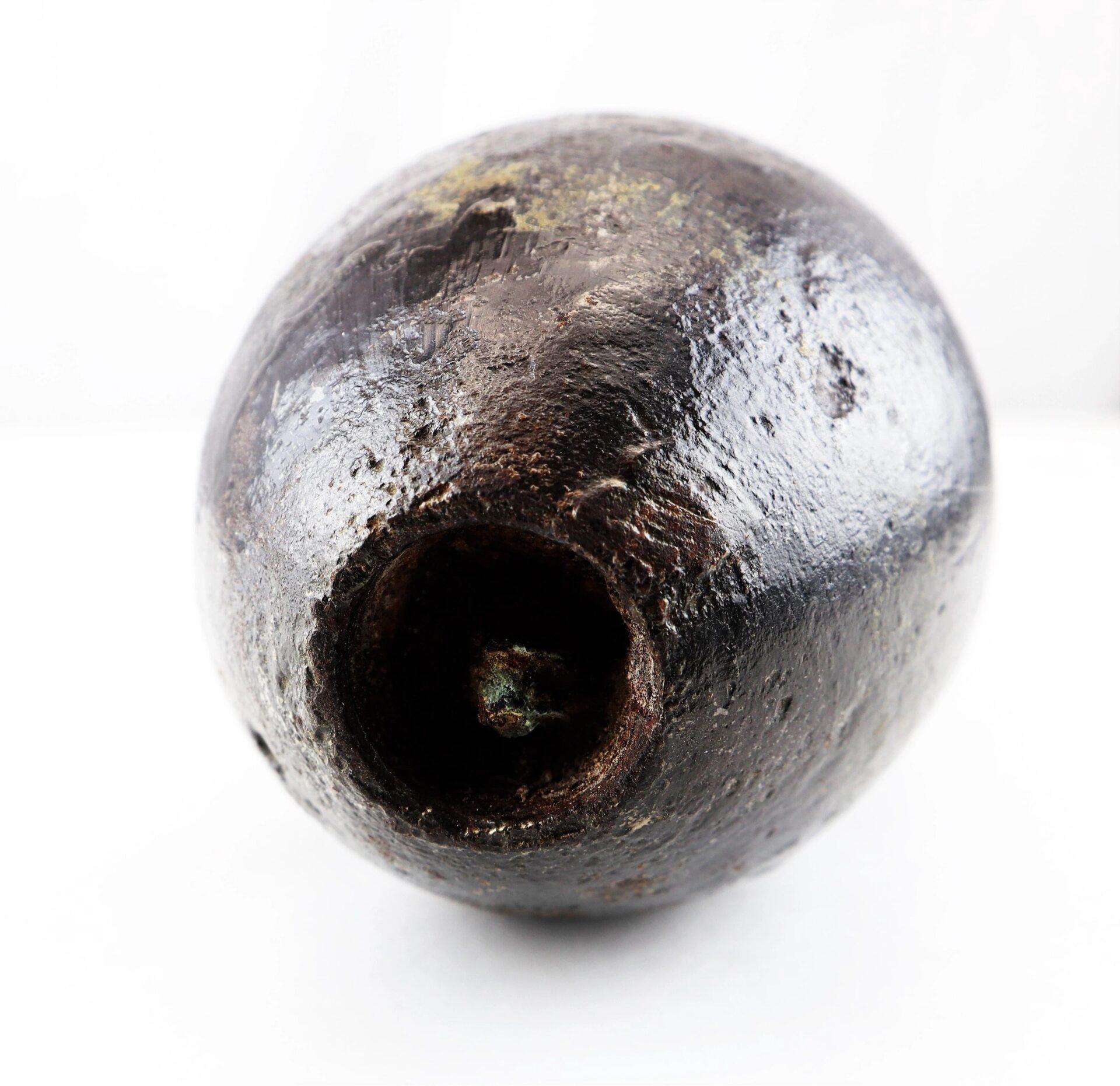 A close-up of a US 4.2” 30-Pounder Parrott Common Shell, a round, dark metallic cannonball with a hollow cavity on one side, shown against a plain white background.