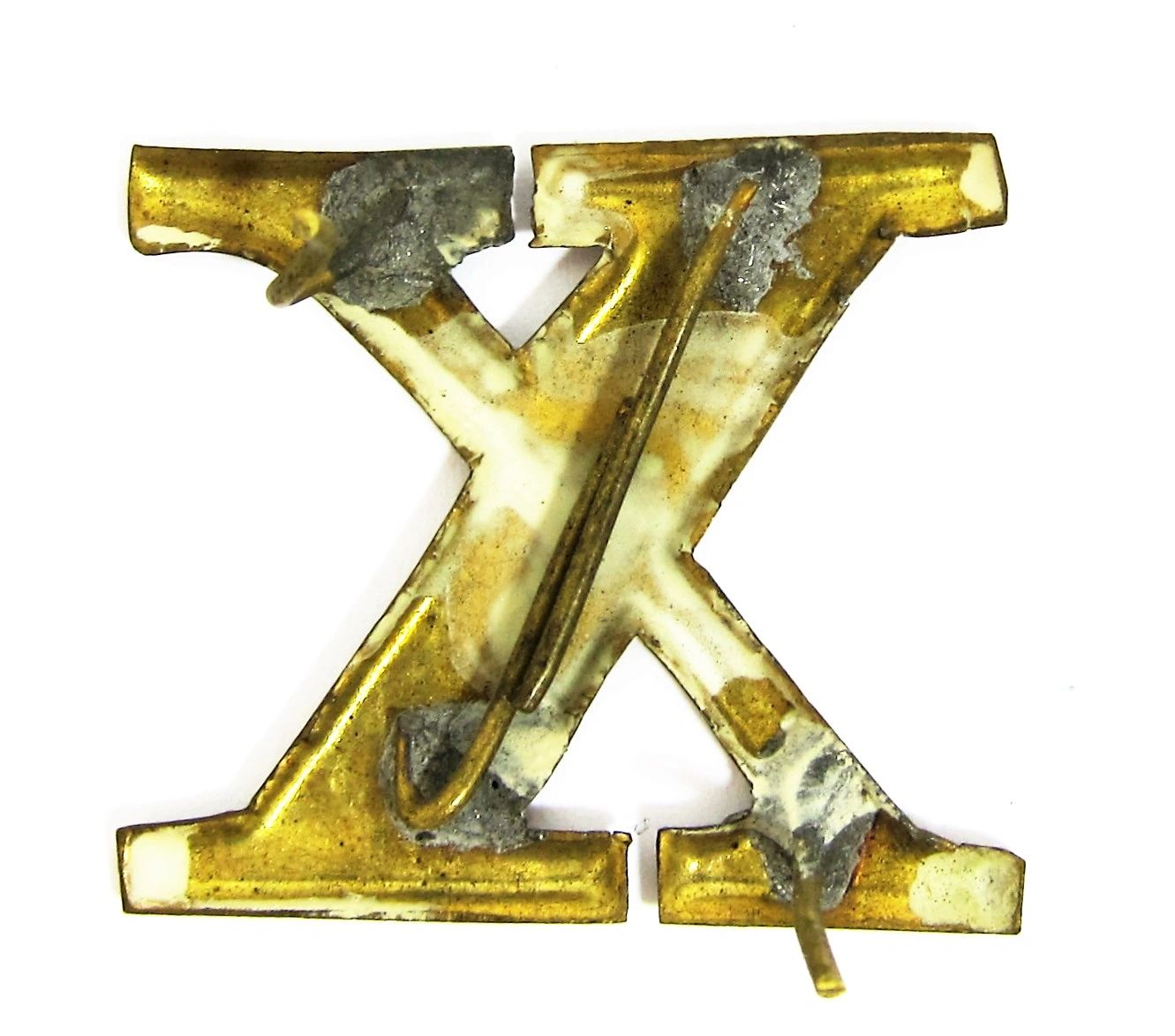 The Regimental Company Letter X is a worn, gold-colored metal piece featuring visible scratches, tarnish, and some adhesive residue on its surface.