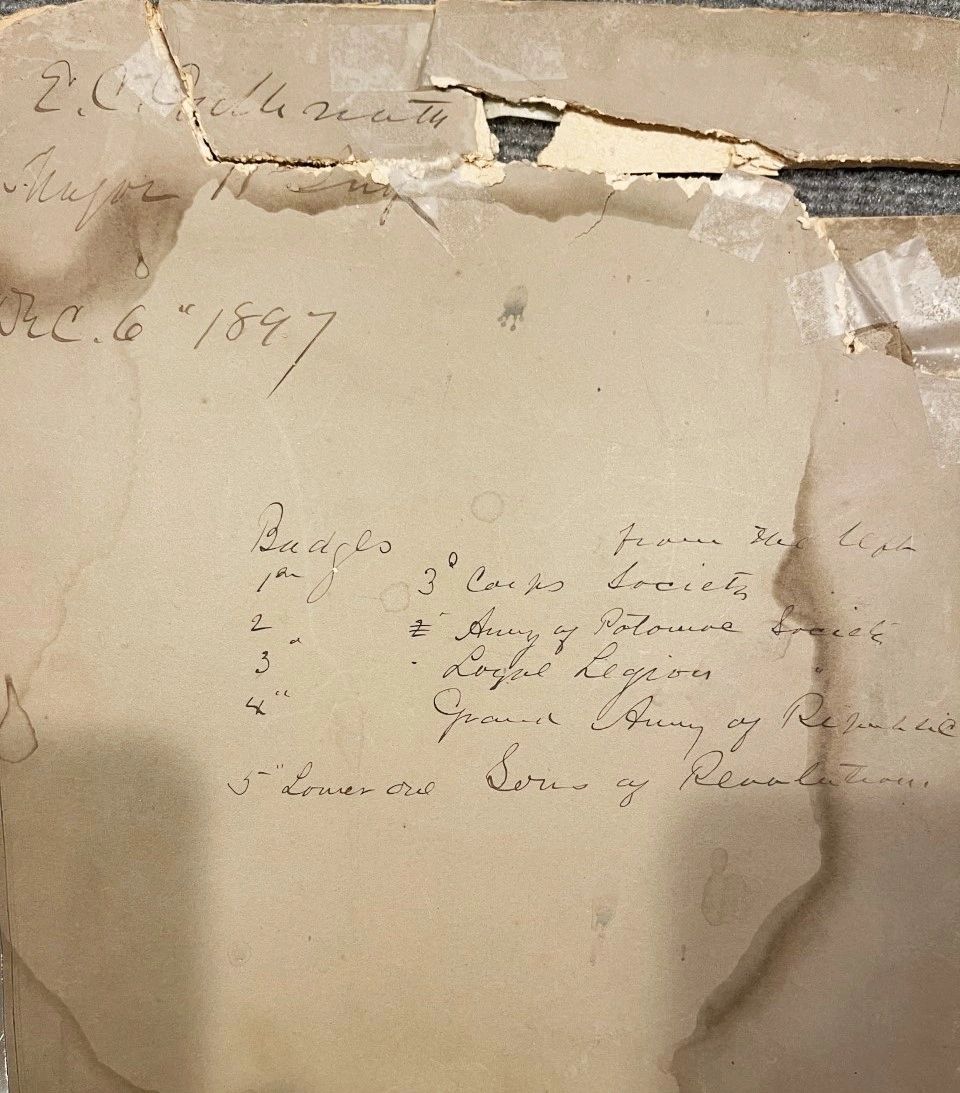 A torn, aged paper with handwritten notes listing badges and organizations for Major Erasmus Corwin Gilbreath, dated Dec. 6, 1897. The top edge is cracked and damaged.