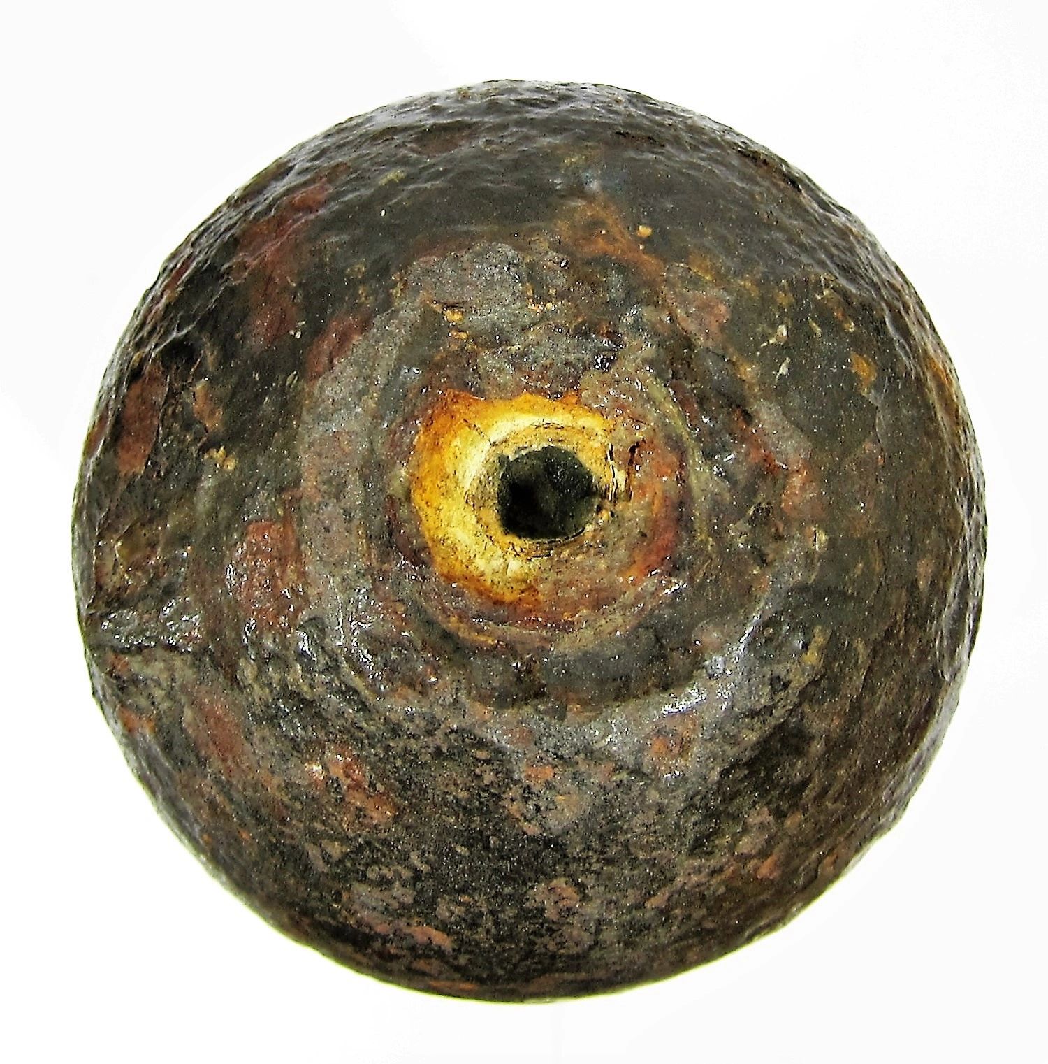 A close-up of a Confederate Read / Sold cannonball, round and weathered with rust and a central hole, set against a white background.