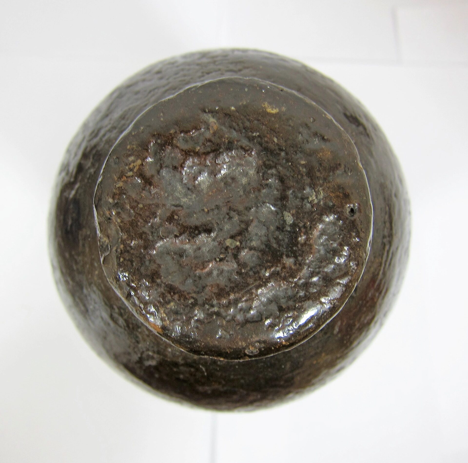 A close-up view of the base of a dark, rusted US 30 Pound Parrott Chilled Nose Bolt, likely an old iron artillery round, placed on a white surface.