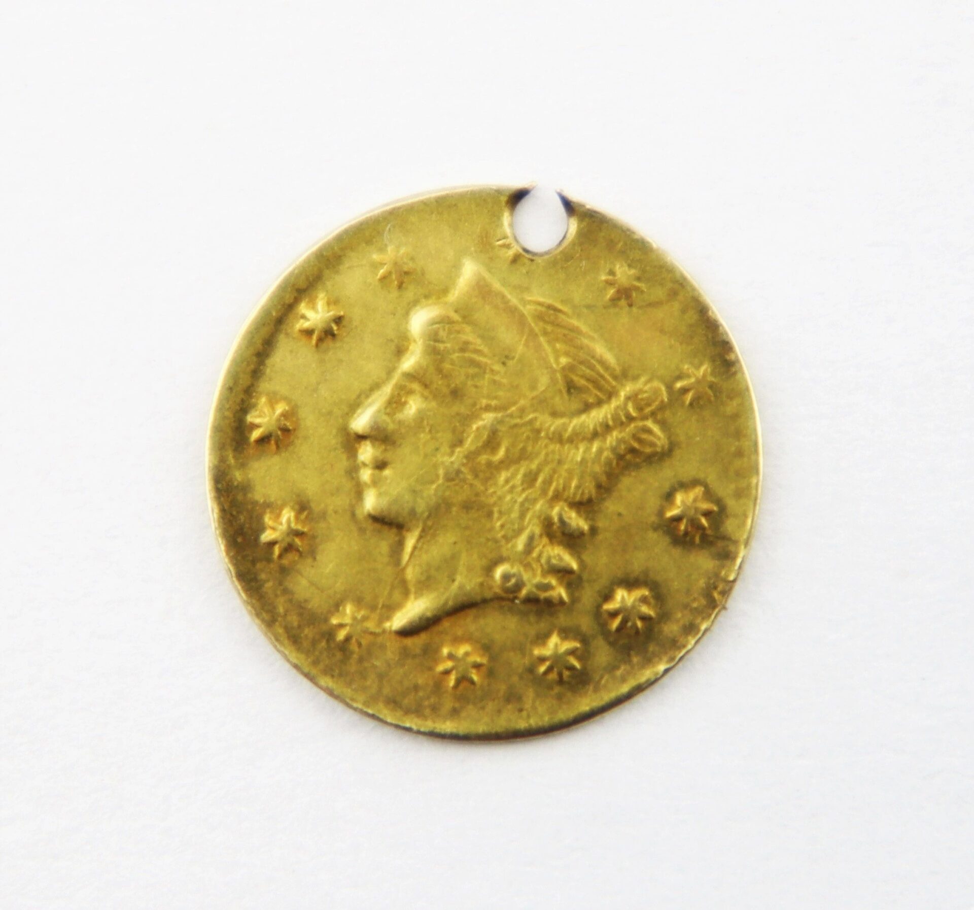 An 1860 Quarter Dollar Gold Coin featuring a woman's profile surrounded by stars, with a small hole near the edge, shown on a white background.