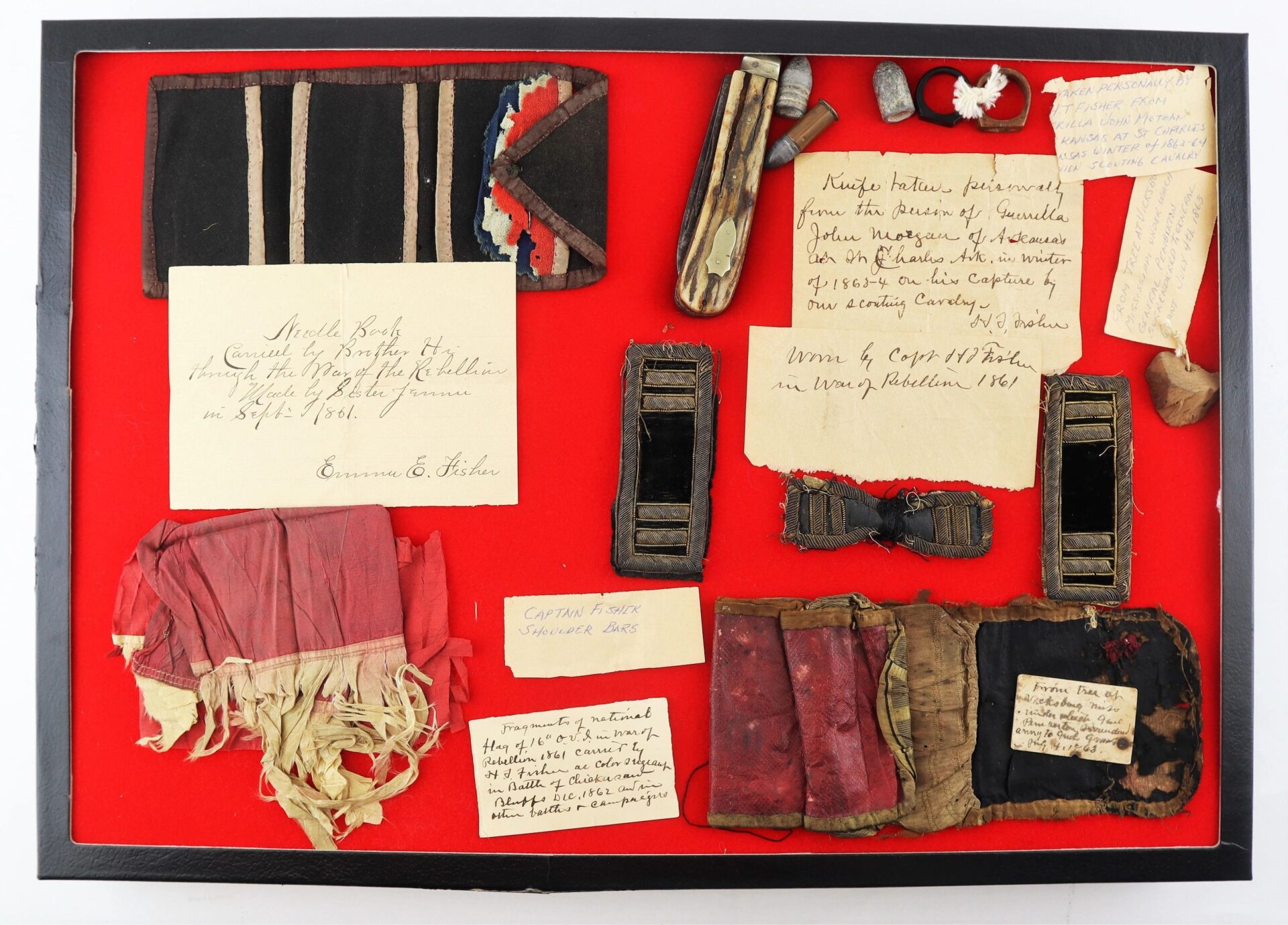 A display case featuring the John Hunt Morgan Knife and Grouping ID’d to Hiram T. Fisher, 16th Ohio and 53rd USCT—including Civil War-era ribbons, fabric, metal badges, handwritten labels, and epaulettes on a red background.