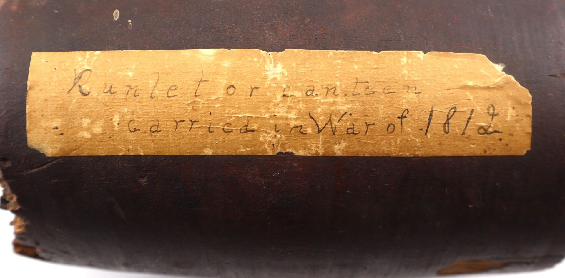 A close-up shows a worn paper label on a dark object with faded handwriting: "War of 1812 Rundlet Canteen / Sold.