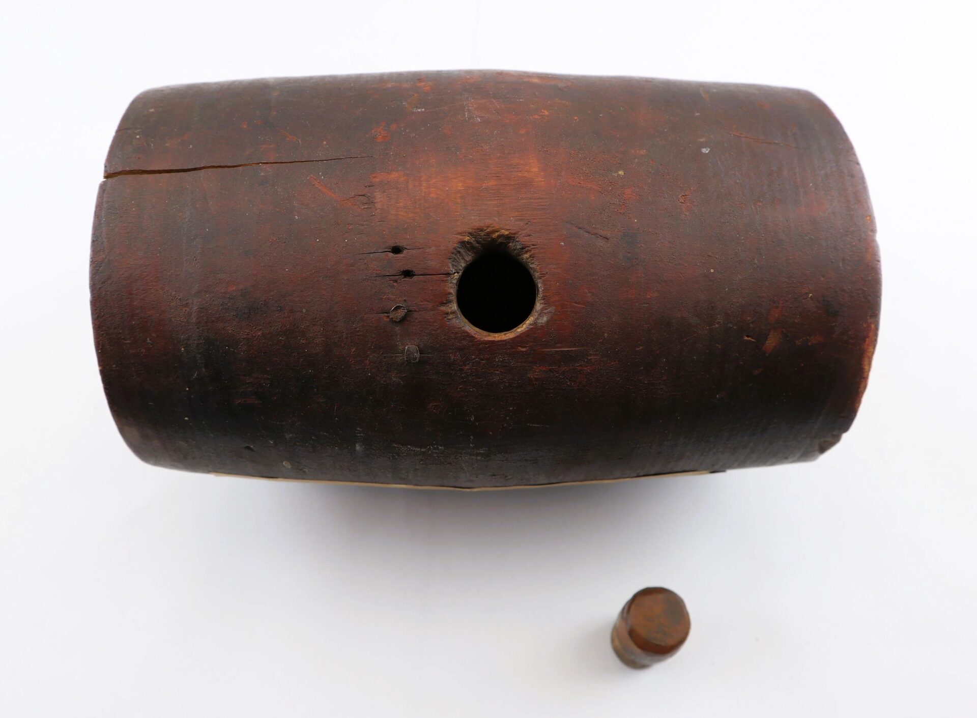 A War of 1812 Rundlet Canteen lies on its side with a hole in the center and a cylindrical wooden stopper placed below it, all set against a white background.