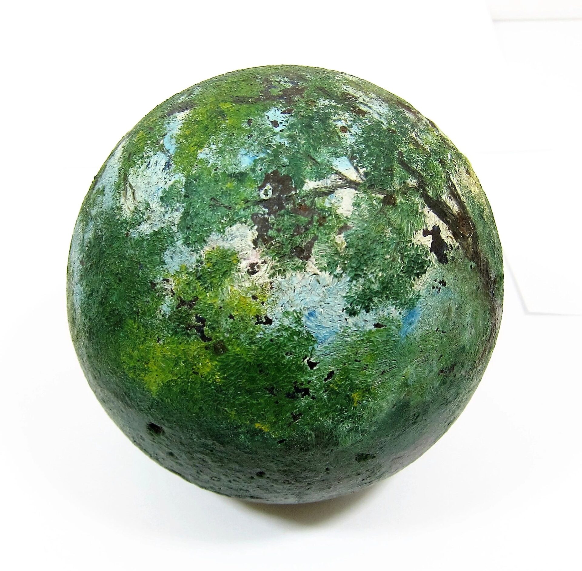 The Painted Cannon Ball features a spherical shape with a green landscape, trees, and a blue sky hand-painted on a white background.
