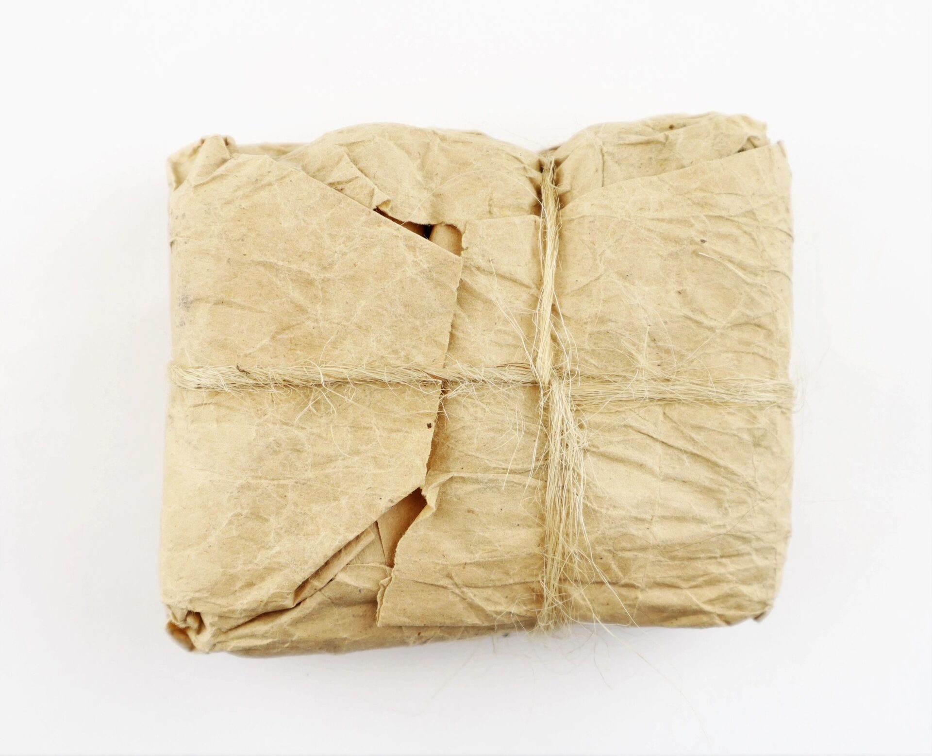 An unopened pack of .58 caliber Minie ball cartridges, wrapped in crumpled brown paper and tied with twine, set against a plain white background.