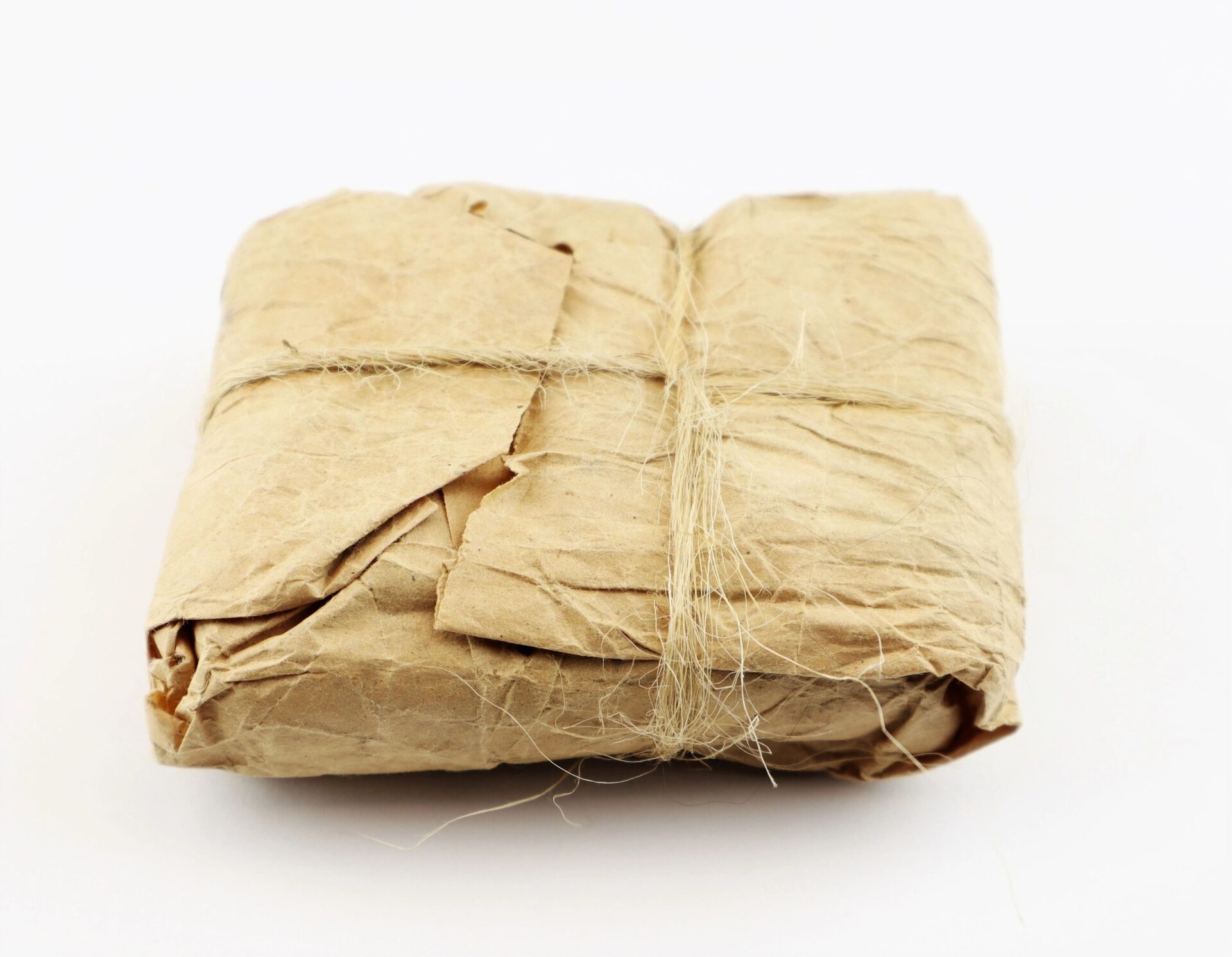 An unopened pack of .58 caliber Minie Ball cartridges, wrapped in crinkled brown paper and tied with rough twine, rests on a plain white background.