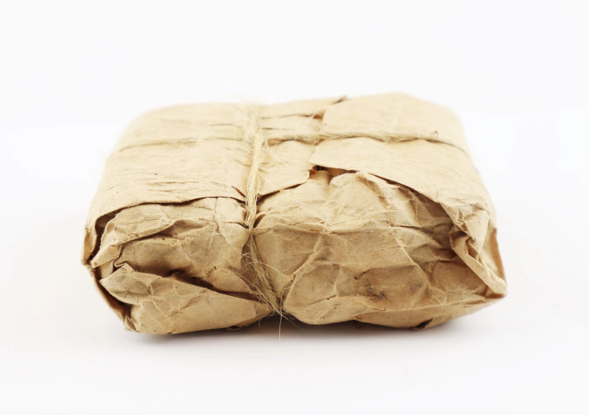 An unopened pack of .58 caliber Minie ball cartridges, wrapped in crumpled brown paper and tied with twine, is displayed against a plain white background.