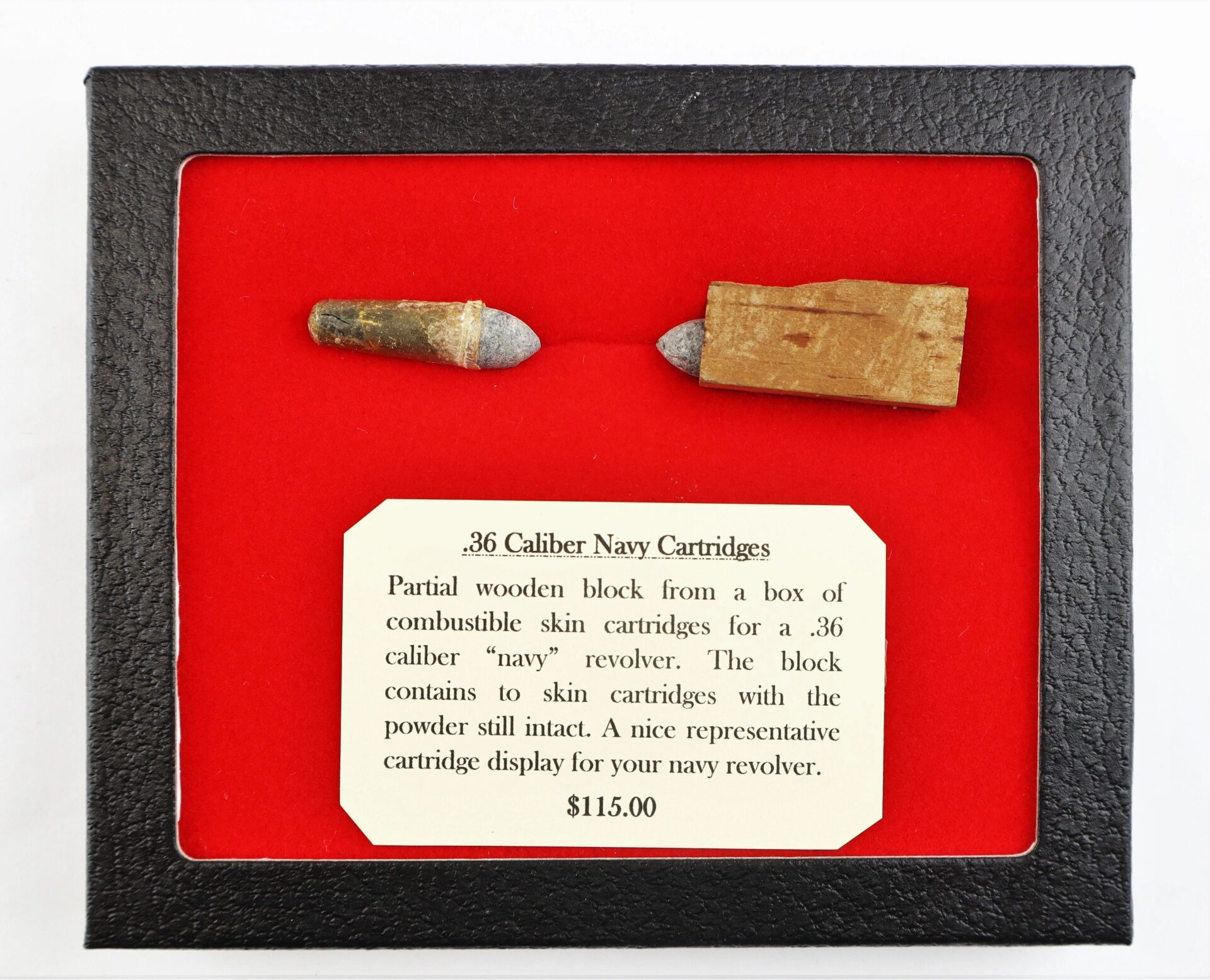 A display case features two .36 Caliber Navy Cartridges, one partially encased in wood, set on a red background with a descriptive label. Product Name: .36 Caliber Navy Cartridges / SOLD.