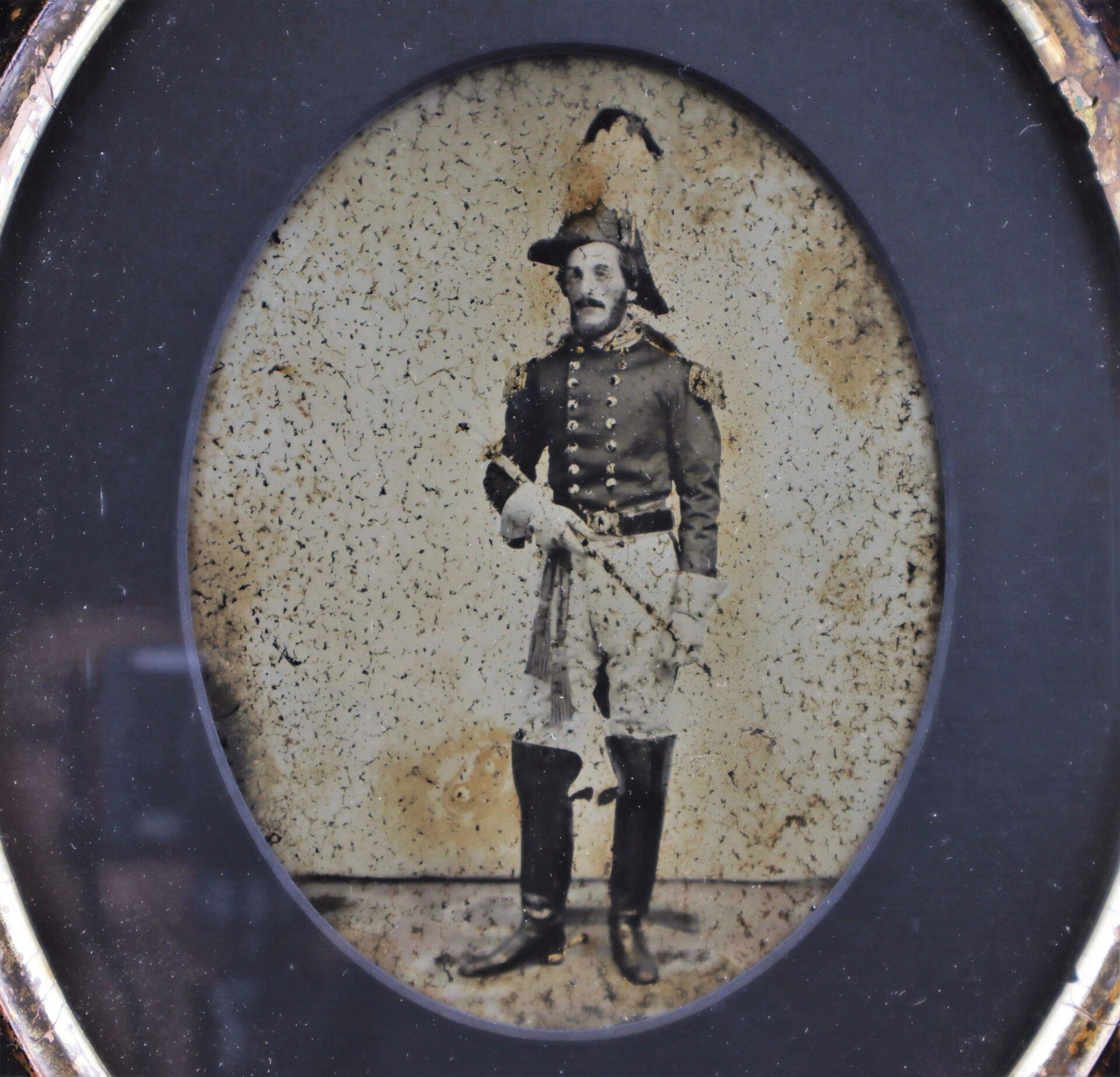 A full plate ambrotype from the 1850s shows a militia officer in uniform, wearing a feathered hat and holding a sword, posed in a studio.