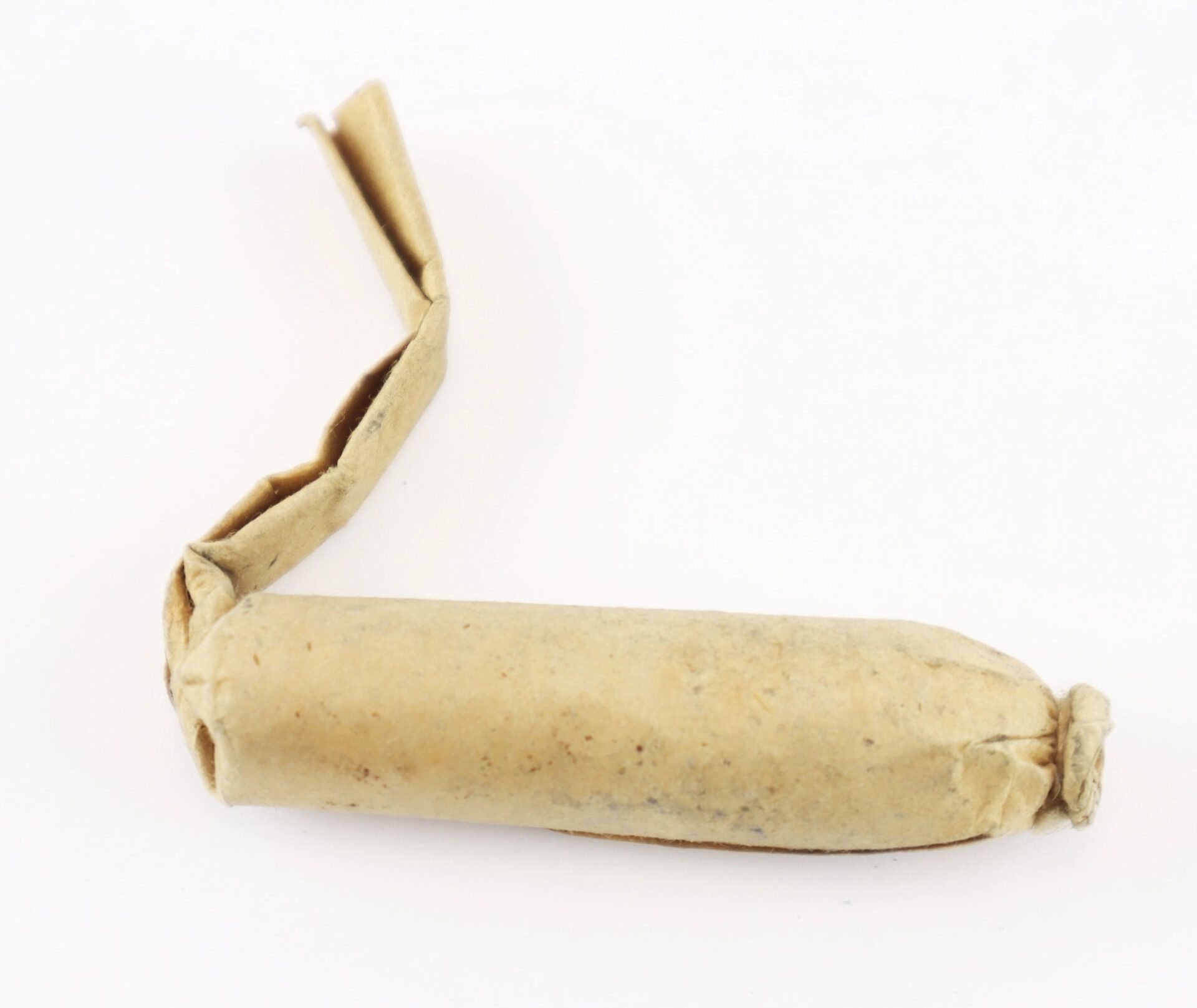 A Civil War .58 Caliber Minie Ball Cartridge, partially unwrapped with one end twisted closed, lies on a white surface. / SOLD.