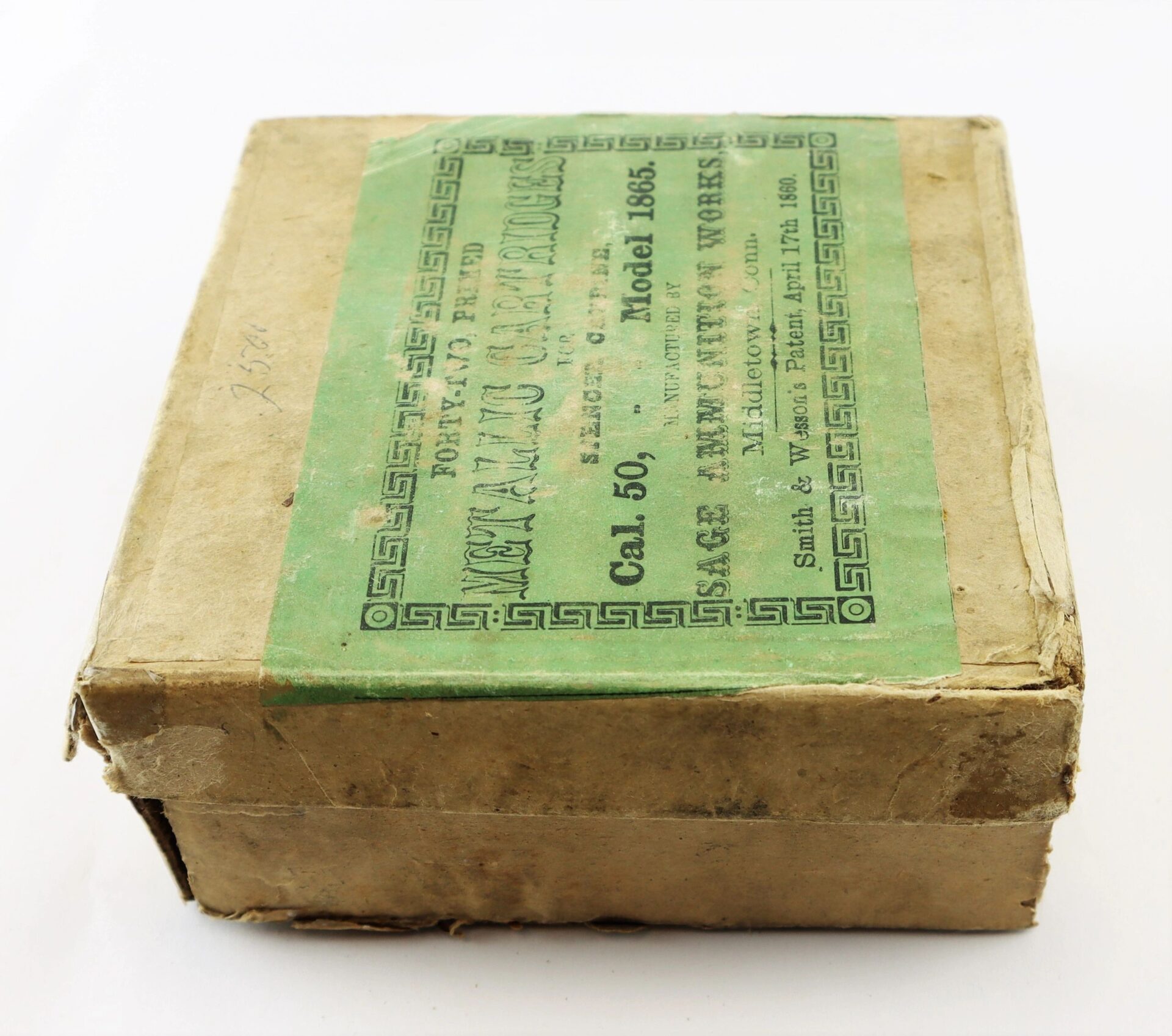 A worn, rectangular cardboard box with a green label reading "Complete Box of 1865 Spencer Cartridges" and manufacturing details printed on the top.