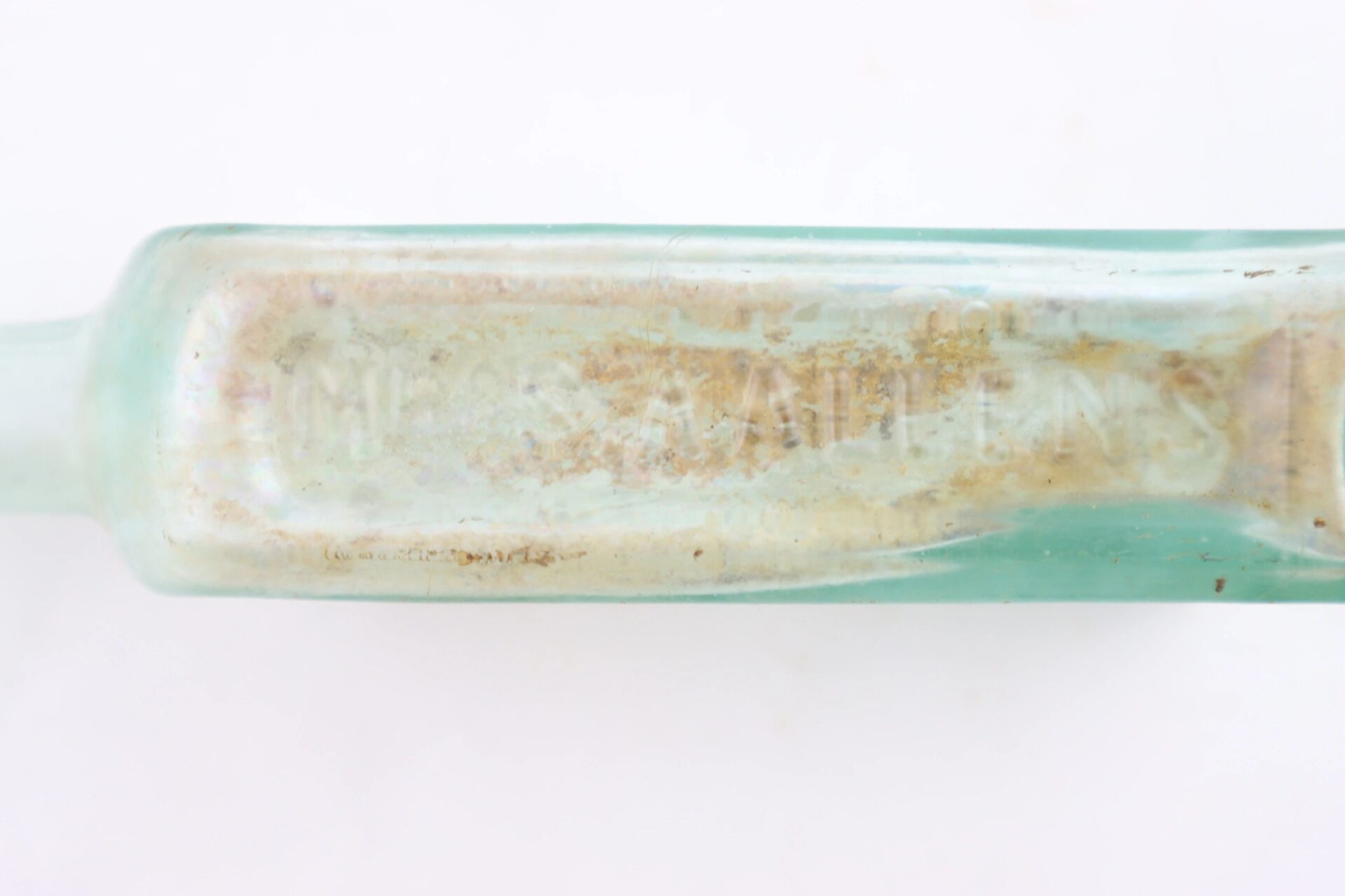 A close-up of a weathered, rectangular Mrs. S.A. Adams Worlds Hair Balsam Bottle from Brandy Station, Virginia, featuring faded and partially obscured embossed text on its glass surface.