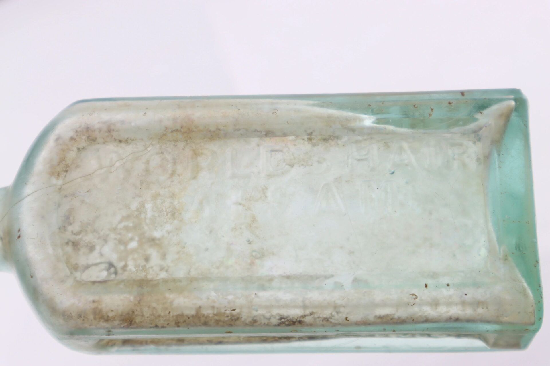 A close-up of an old, rectangular Mrs. S.A. Adams Worlds Hair Balsam bottle from Brandy Station, Virginia, with faded embossed text and visible dirt inside.