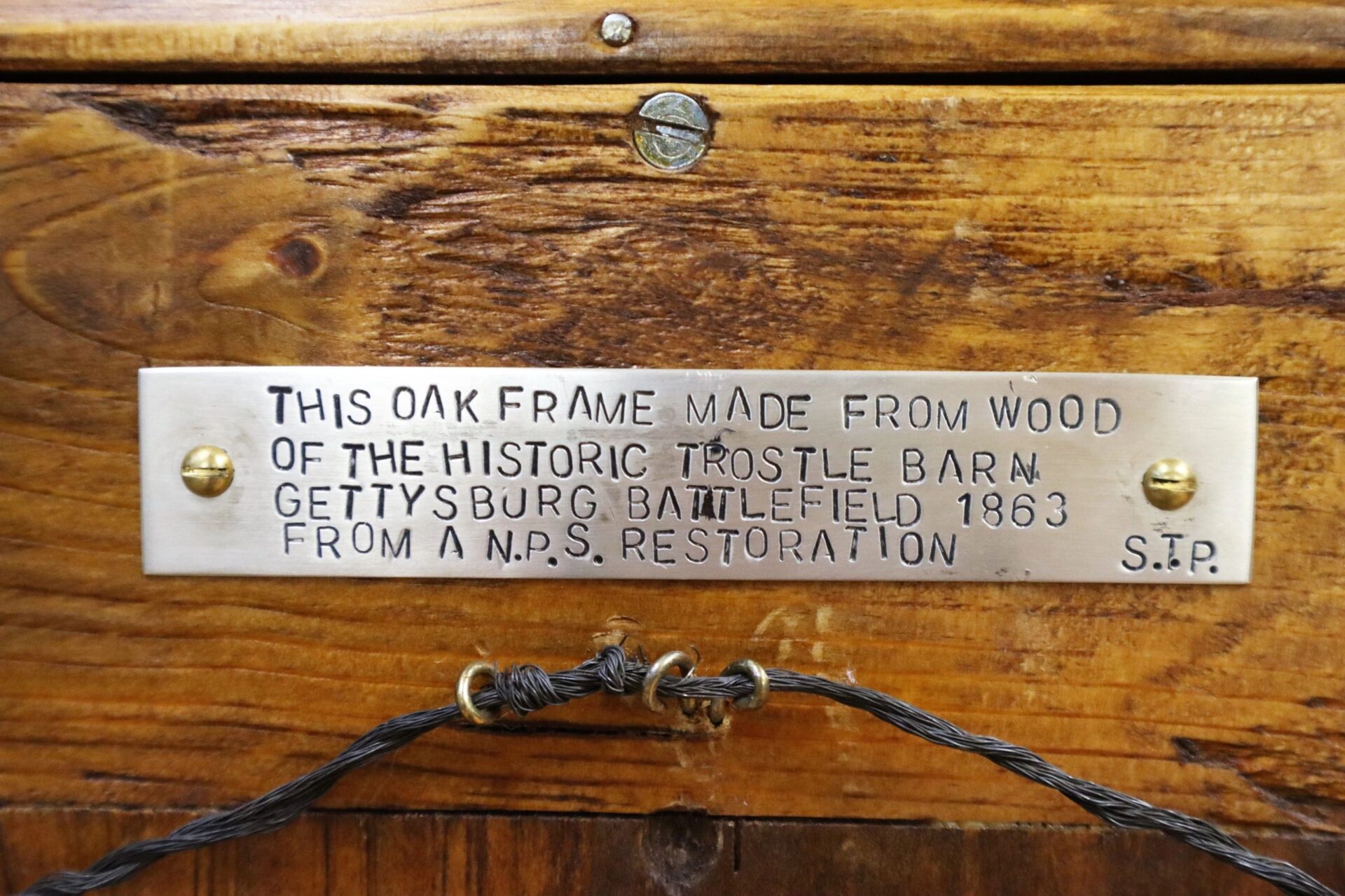 A metal plaque on wood reads: "This oak frame was made from wood of the historic Trostle Barn, Gettysburg Battlefield 1863, holding a Flank Marker Flag of the 2nd Regiment NY State Militia (82nd NY Infantry), Antietam & Gettysburg.