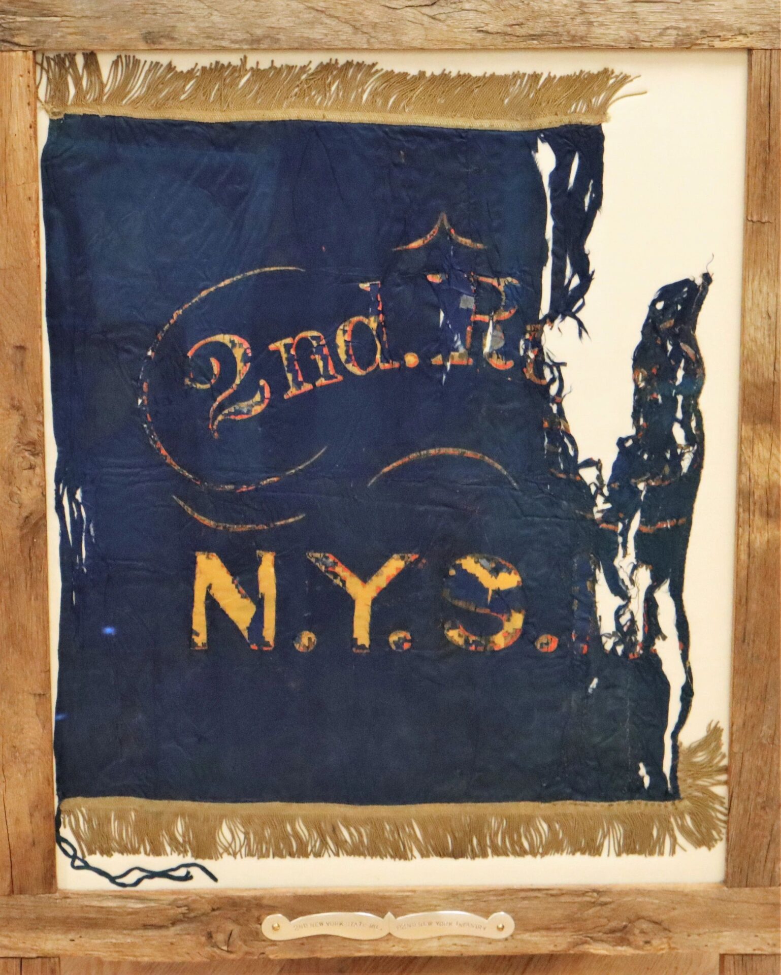 A tattered blue Flank Marker Flag of the 2nd Regiment New York State Militia (82nd NY Infantry), with yellow "2nd. N.Y.S." text, gold fringe, in a wooden frame; used at Antietam and Gettysburg. / SOLD.