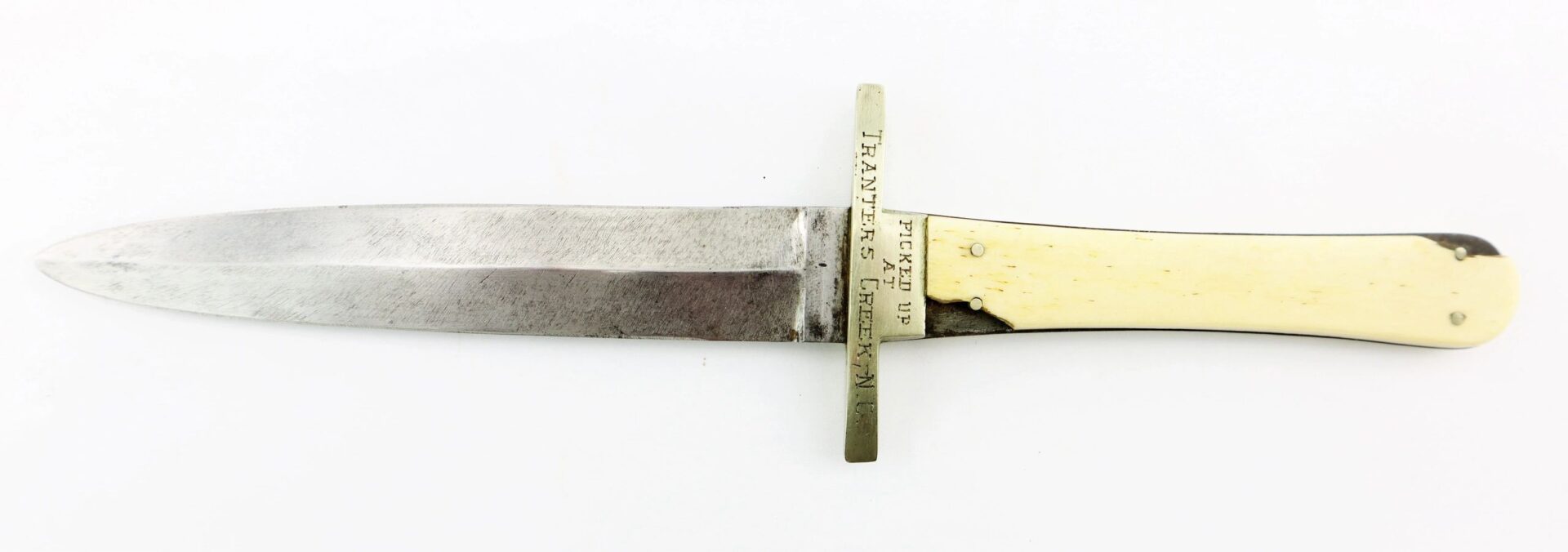 A Sheffield Dagger picked up at Tranter’s Creek, North Carolina by Sgt. George A. Colton, 3rd NY Cavalry/SOD; features a straight metal blade, brass crossguard with inscription, and an ivory or bone-like handle.