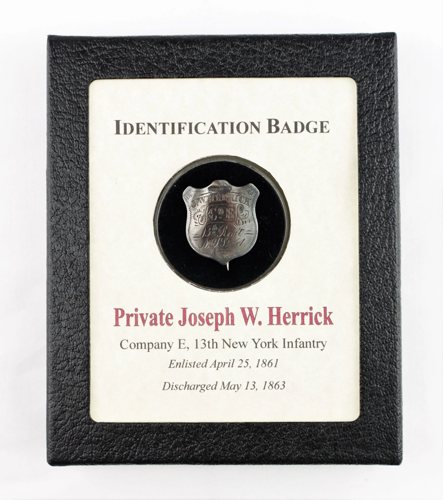 A framed Identification Badge and Discharge of Private Joseph W. Herrick, 13th New York Infantry, displaying his badge with enlistment and discharge dates shown beneath.