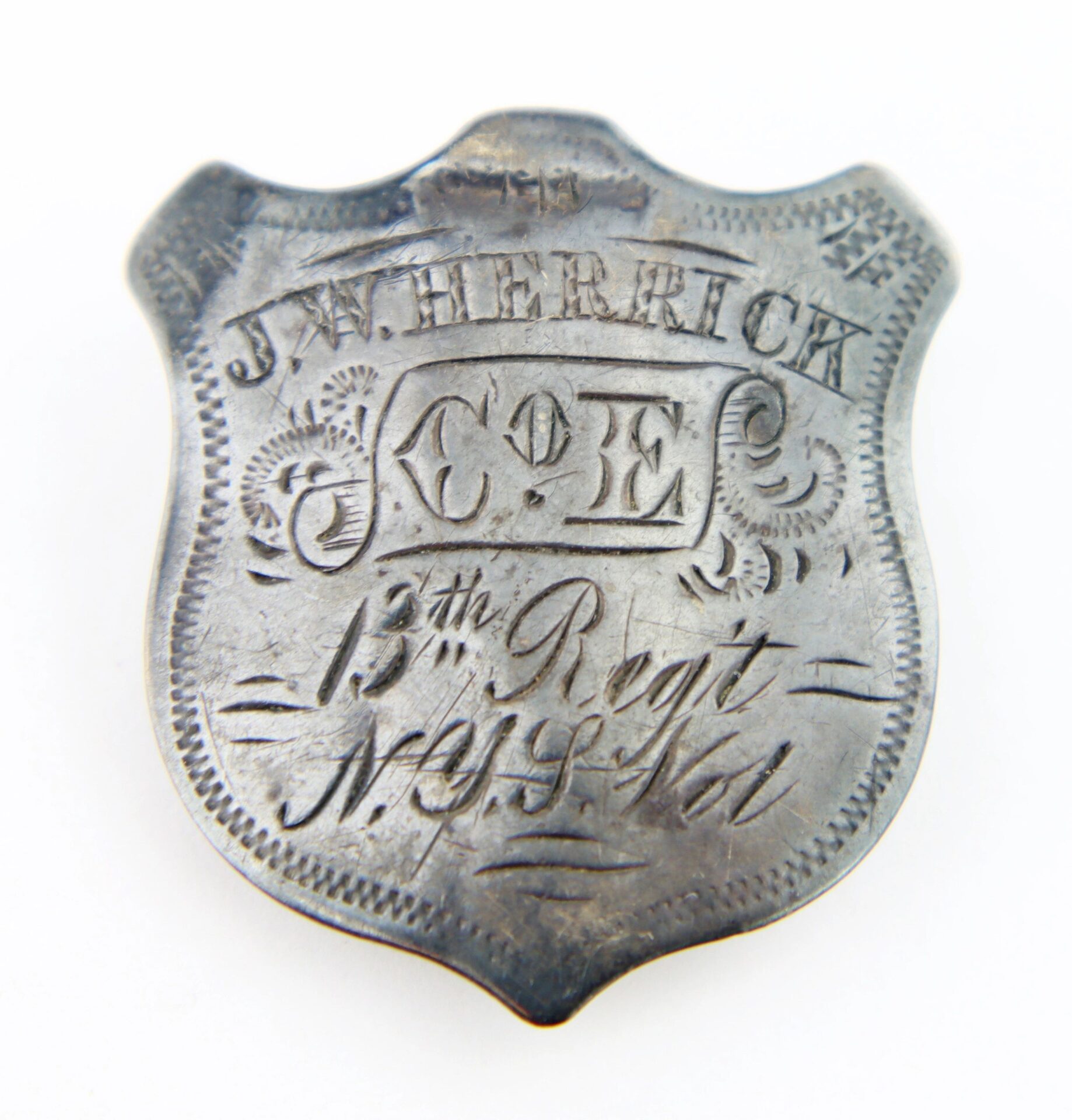 A silver shield-shaped identification badge engraved for Private Joseph W. Herrick, Company E, 13th New York Infantry, featuring decorative detailing.