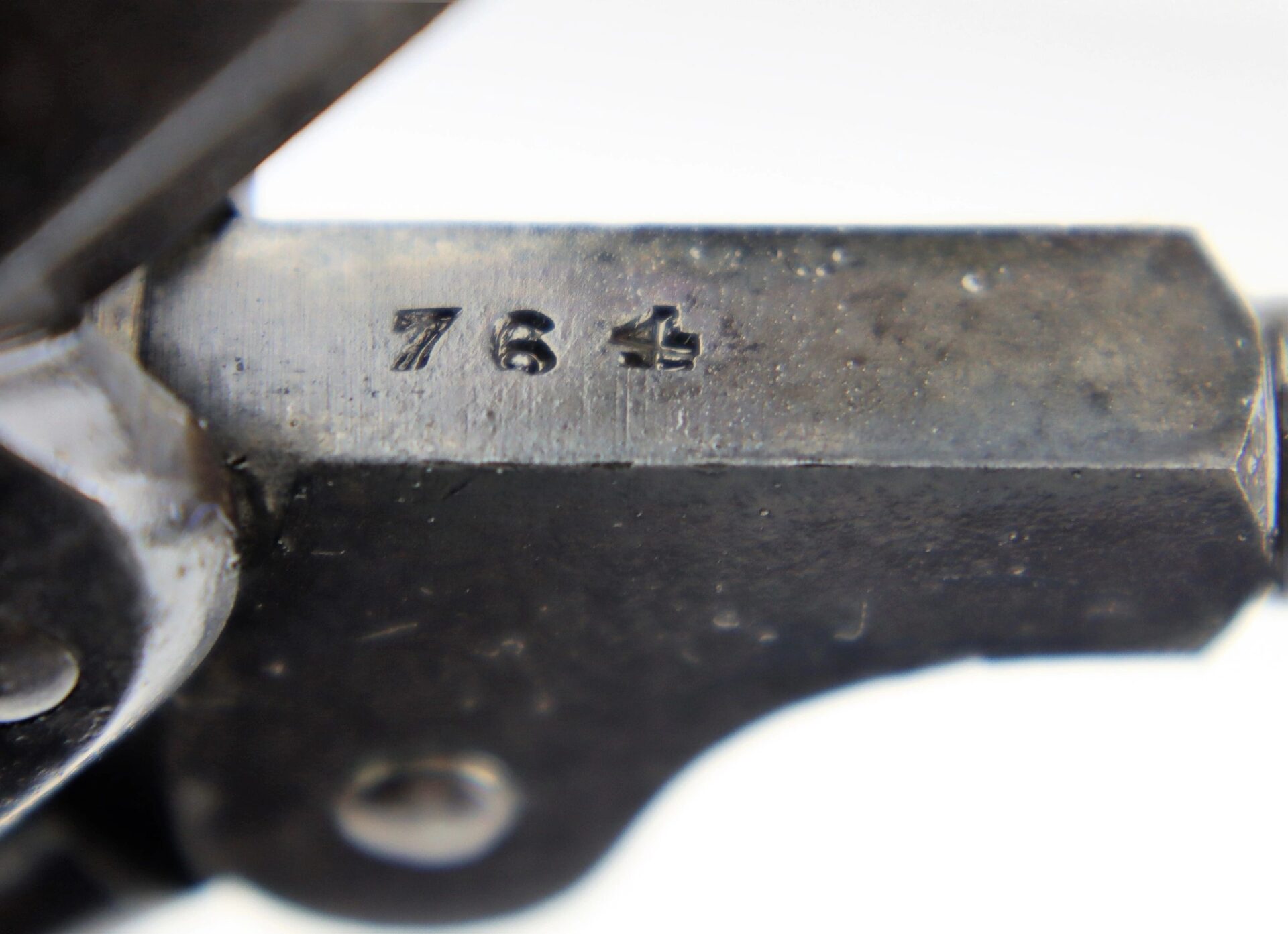 Close-up view of a J. M. Cooper Pocket Model Revolver's metal surface, featuring the numbers "76" and a symbol stamped onto it, with visible signs of wear and use.