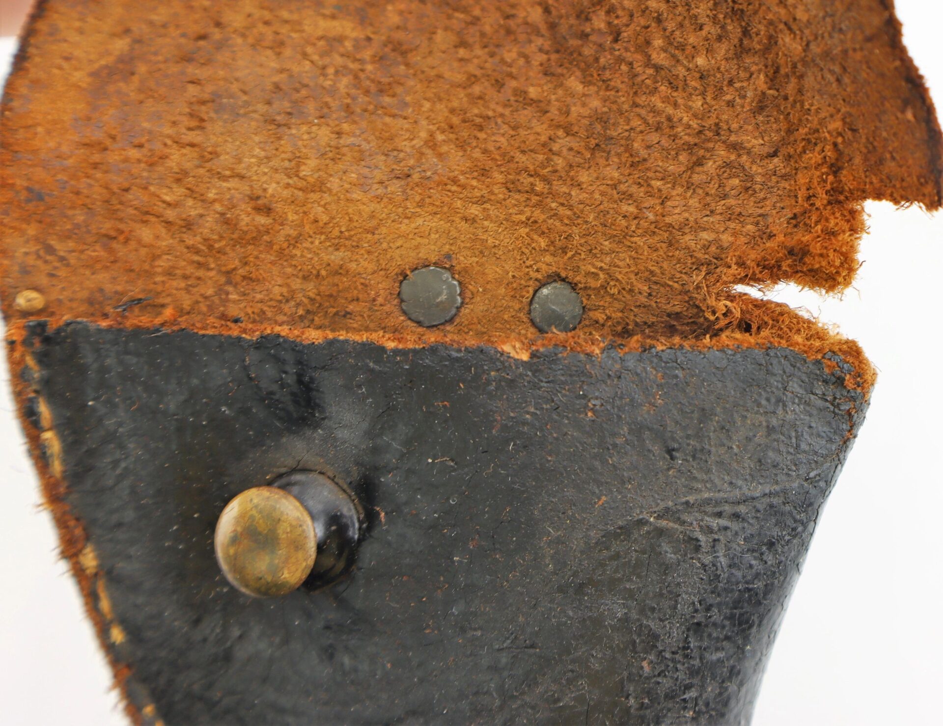 Close-up of a Confederate Holster made of worn leather with rusty rivets, a brass knob, frayed edges, and textured surface.
