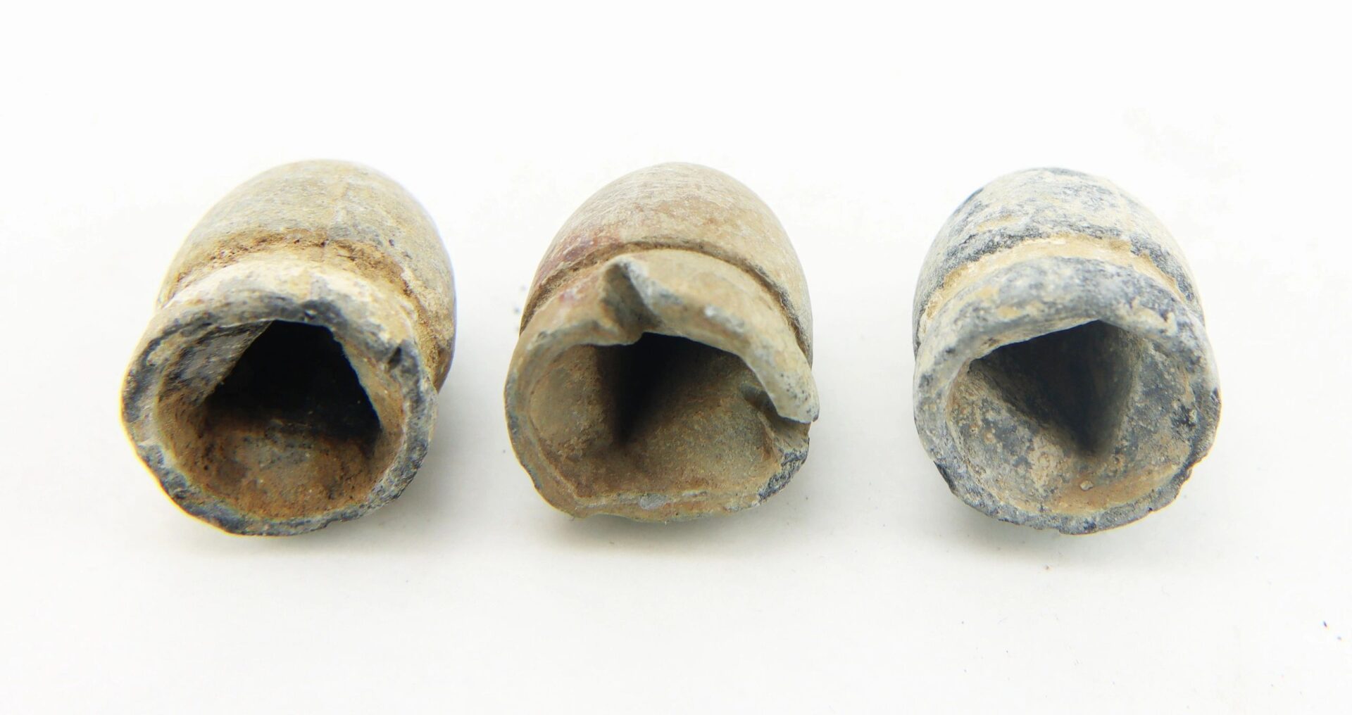Three old, deformed “French Dragoon” Rifle Pattern .69 Caliber lead bullets with hollow bases are arranged side by side on a white background.
