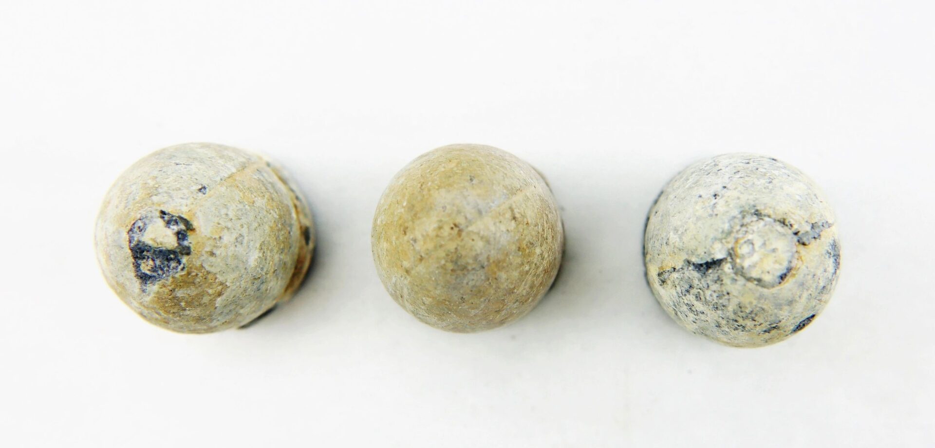 Three “French Dragoon” Rifle Pattern .69 caliber round lead musket balls, weathered, are arranged in a row on a plain white background.