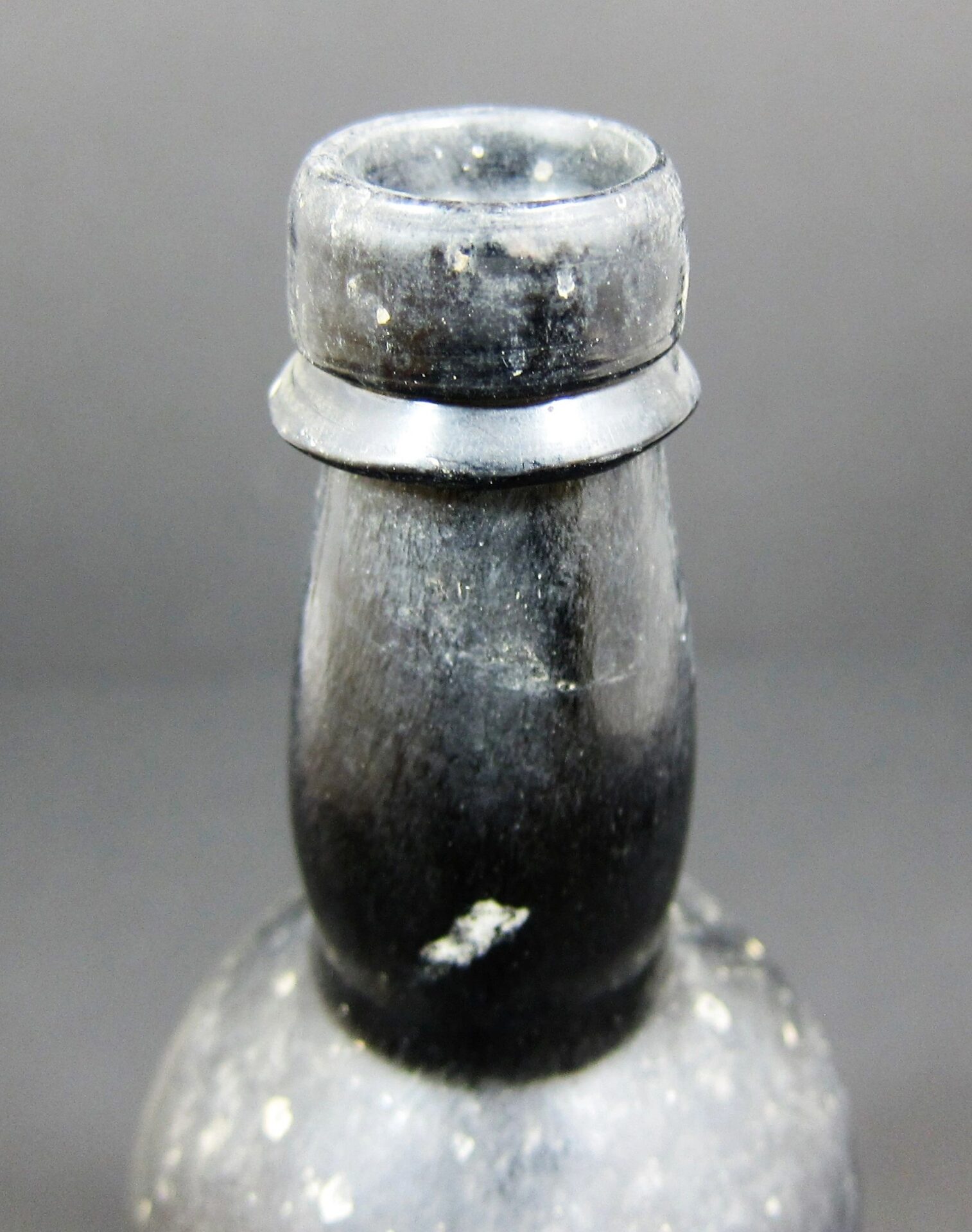 Close-up of the neck and lip of a 19th Century Beer Bottle - Non Excavated, showing its visibly textured, aged black glass surface against a plain gray background.