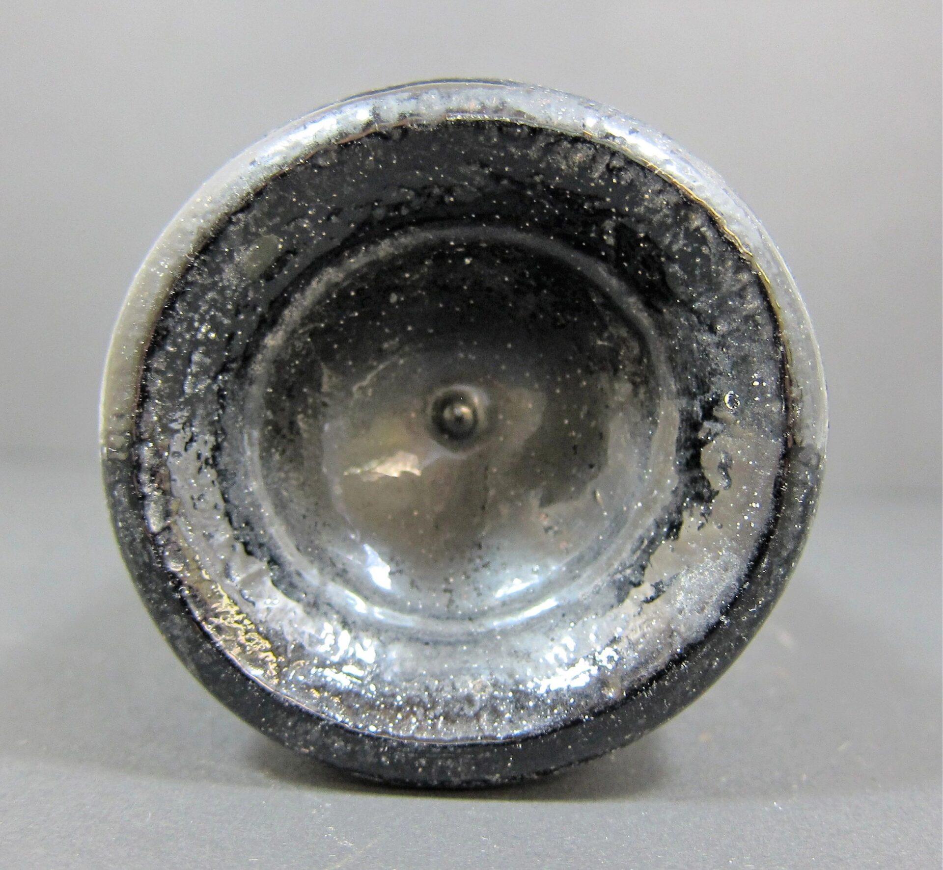 Close-up of the base of a 19th Century Beer Bottle - Non Excavated, showing its black glass, concave bottom, and visible residue or crystallization on the inner surface.